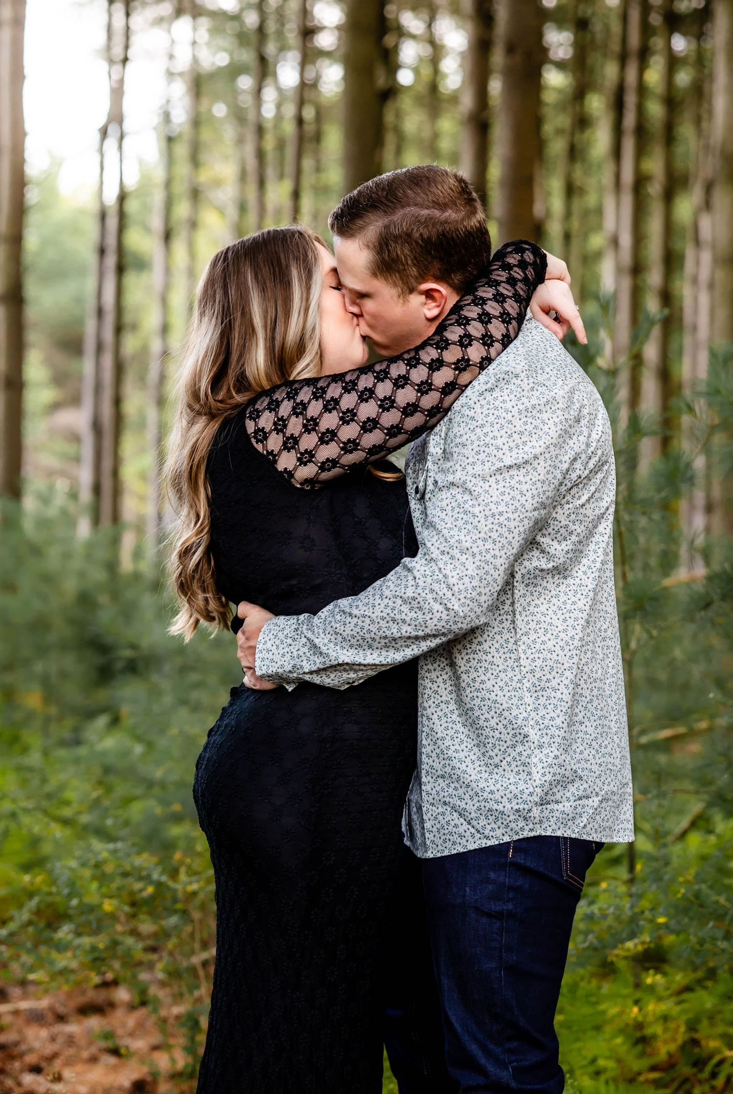 Couple sharing a romantic kiss in a sunlit forest clearing.