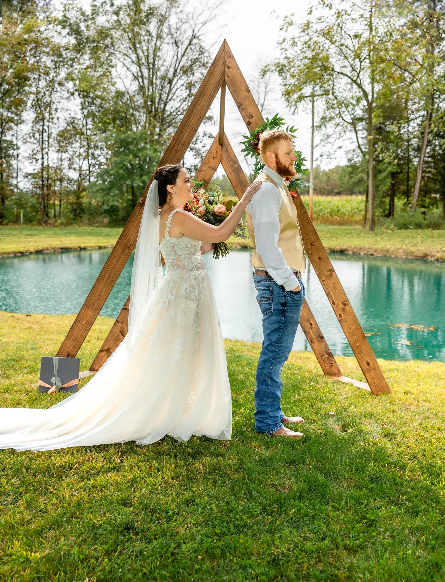Couple posing by a wooden triangle arch with a turquoise pond in the background.