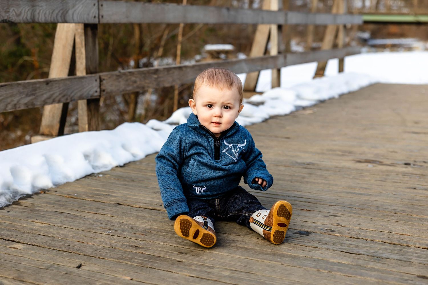 Smiling toddler in blue sweater sitting on wooden boardwalk.