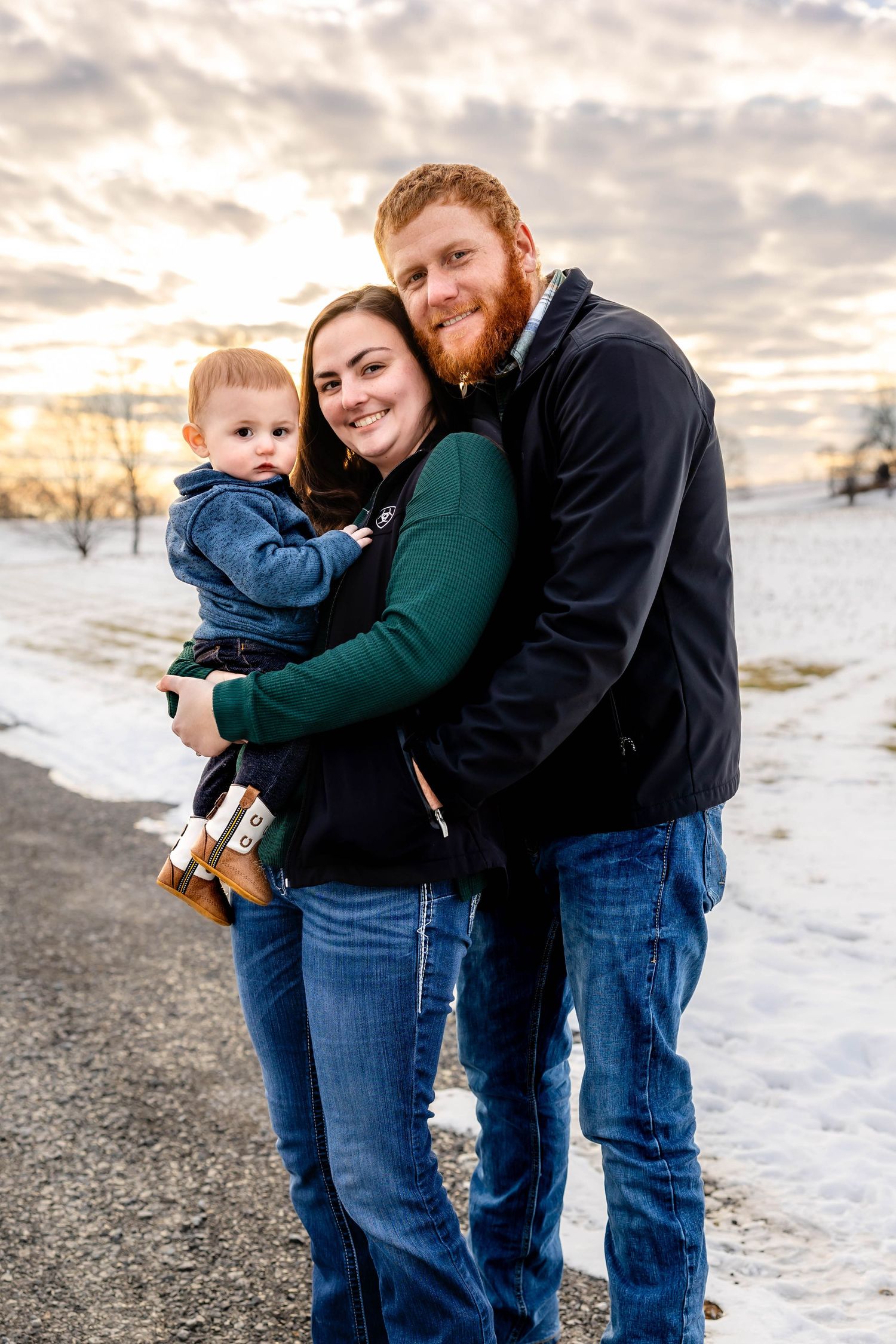 A family poses together on a snowy winter path during sunset with dramatic clouds overhead.