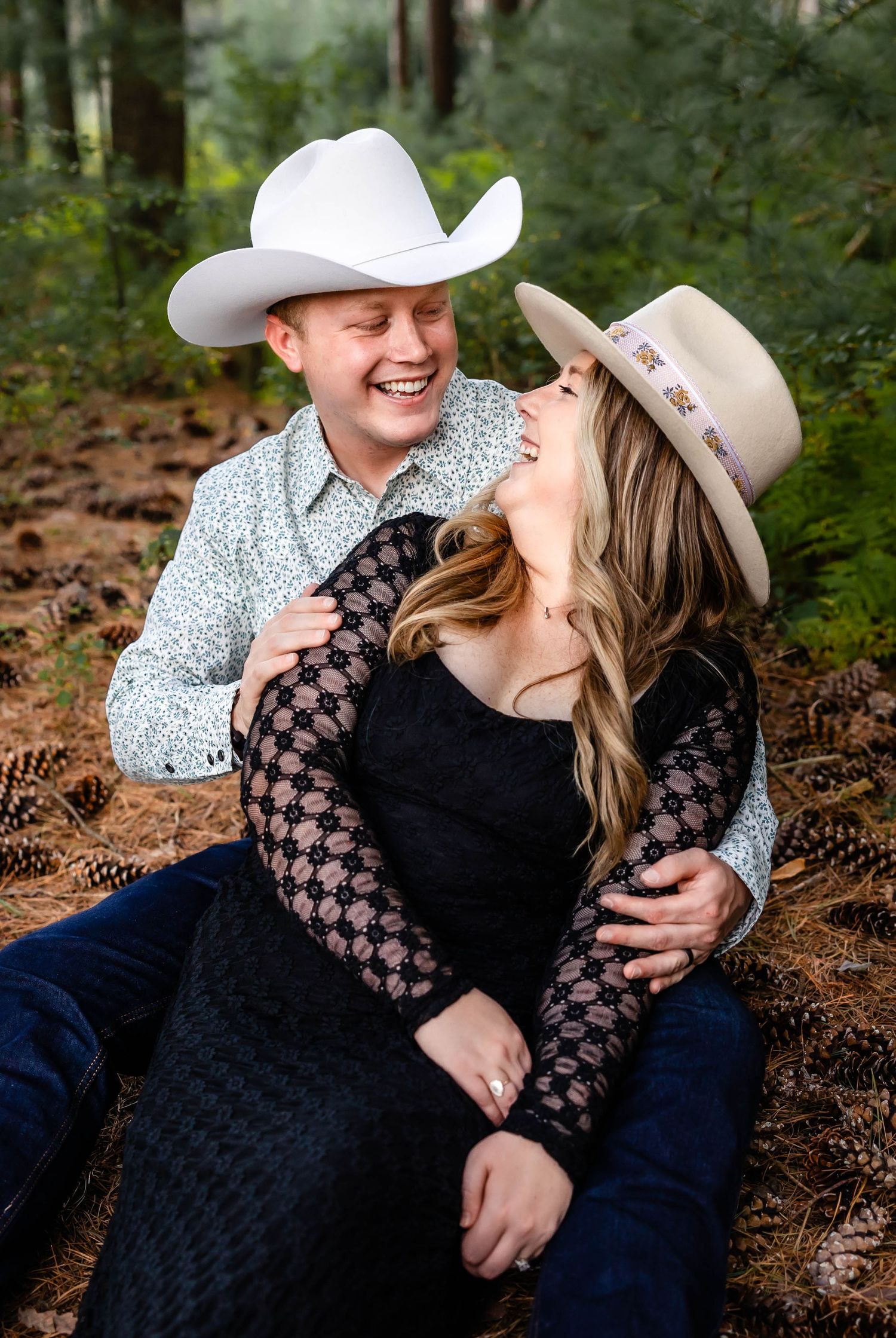 Romantic couple in western attire laugh together during forest photoshoot session.