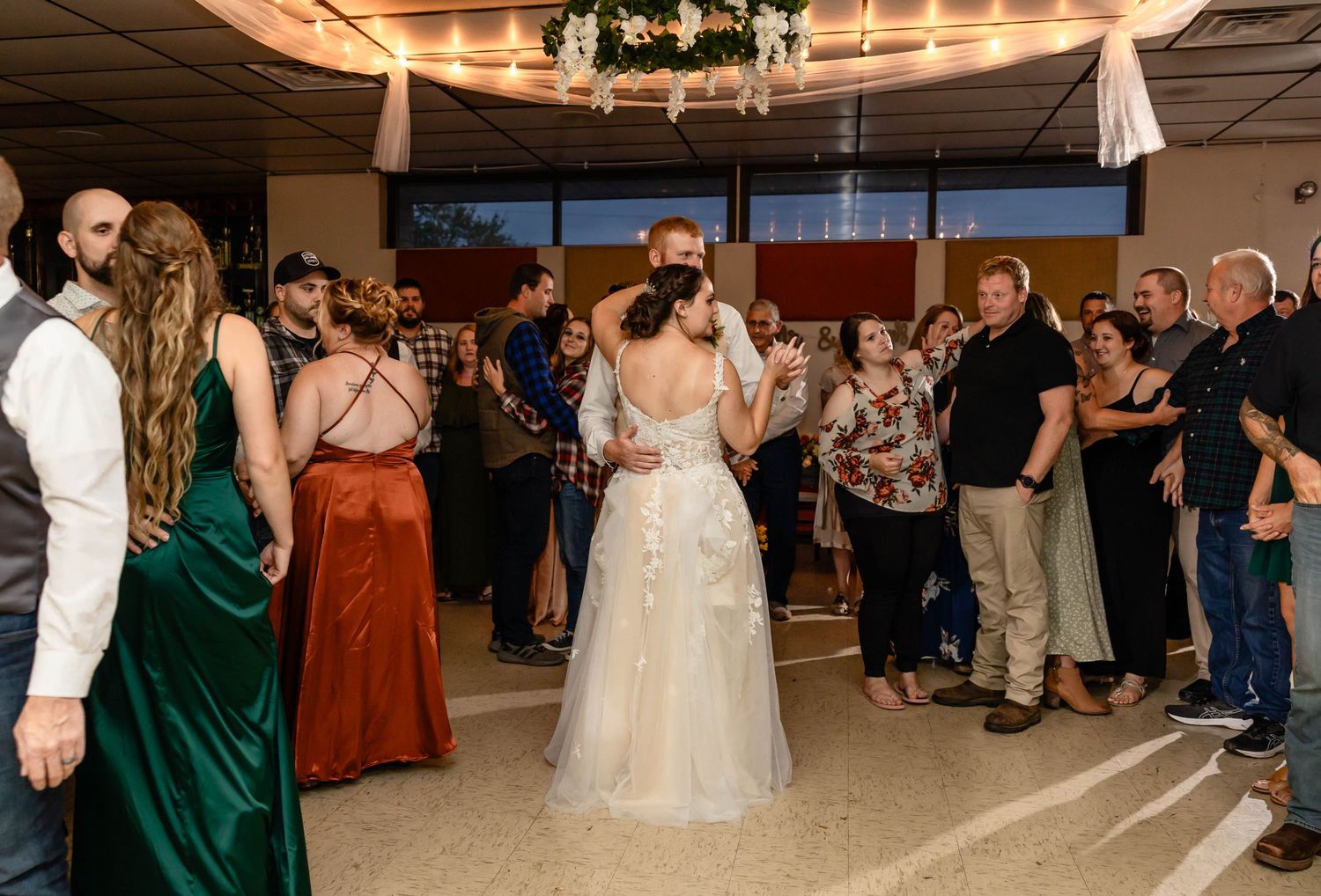 Wedding reception dance floor filled with guests celebrating around bride in white lace gown.