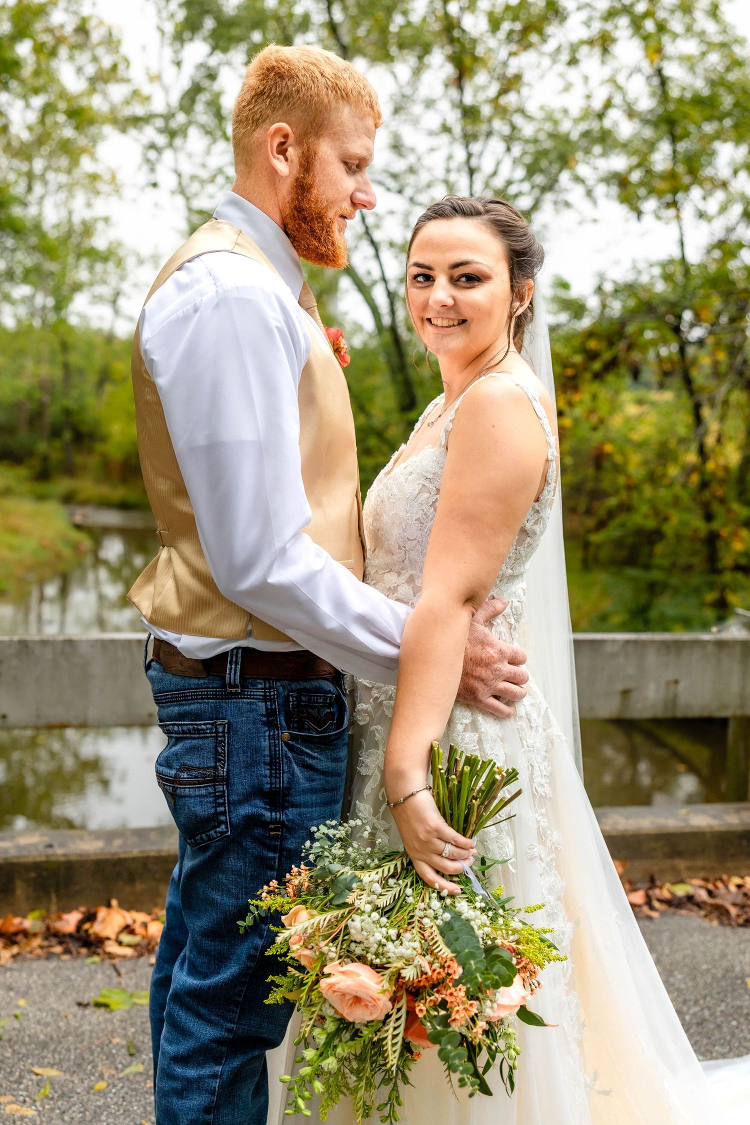 Casual country wedding couple shares an intimate moment on a bridge with autumn scenery.