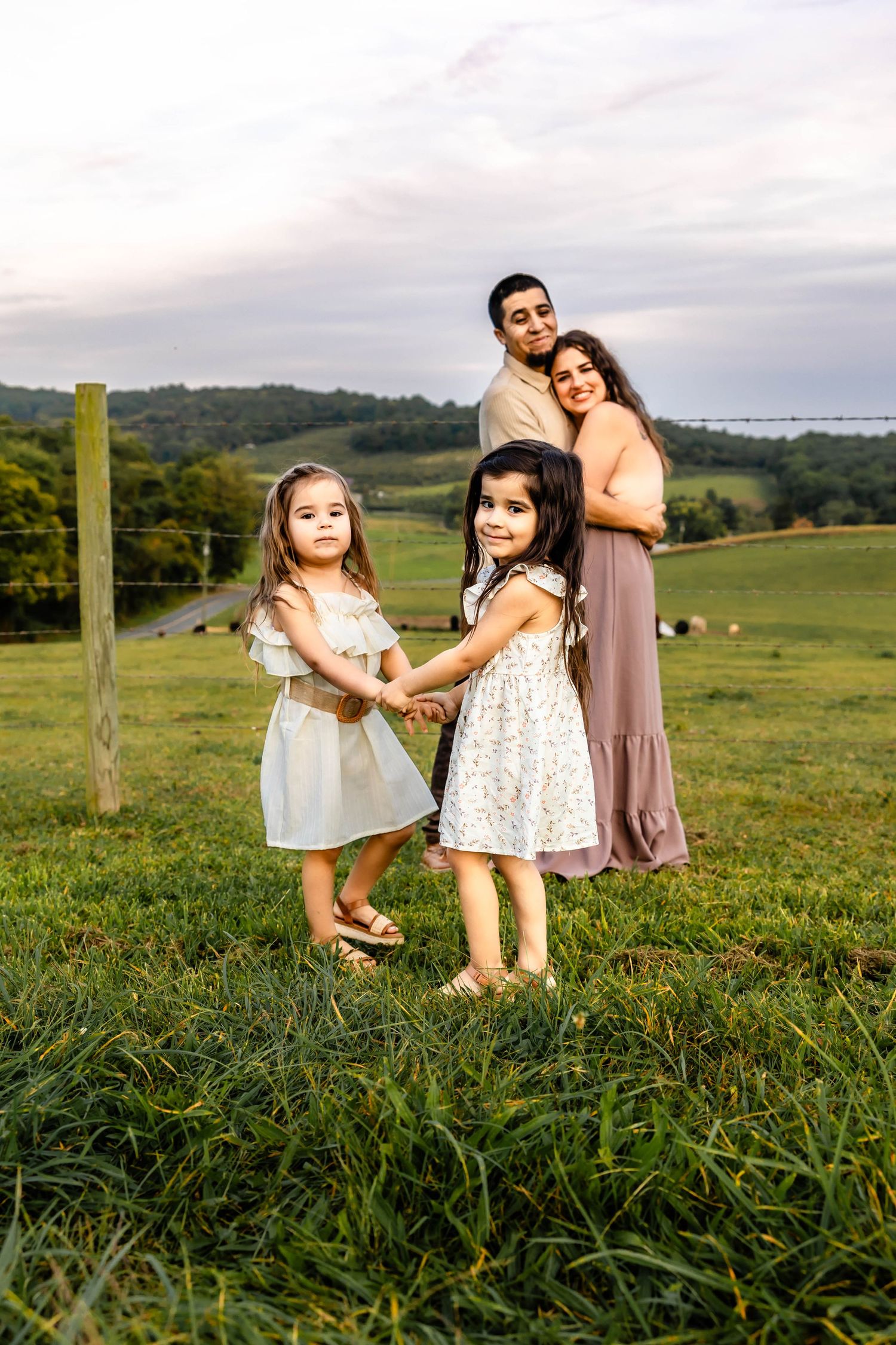 A family portrait on a grassy hillside with rolling farmland and fence posts in the background.