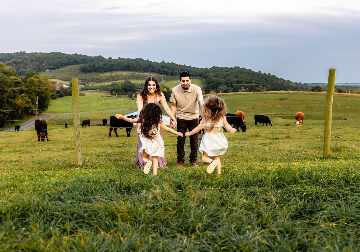 A family jumps together in a scenic field with black cattle grazing in the background.