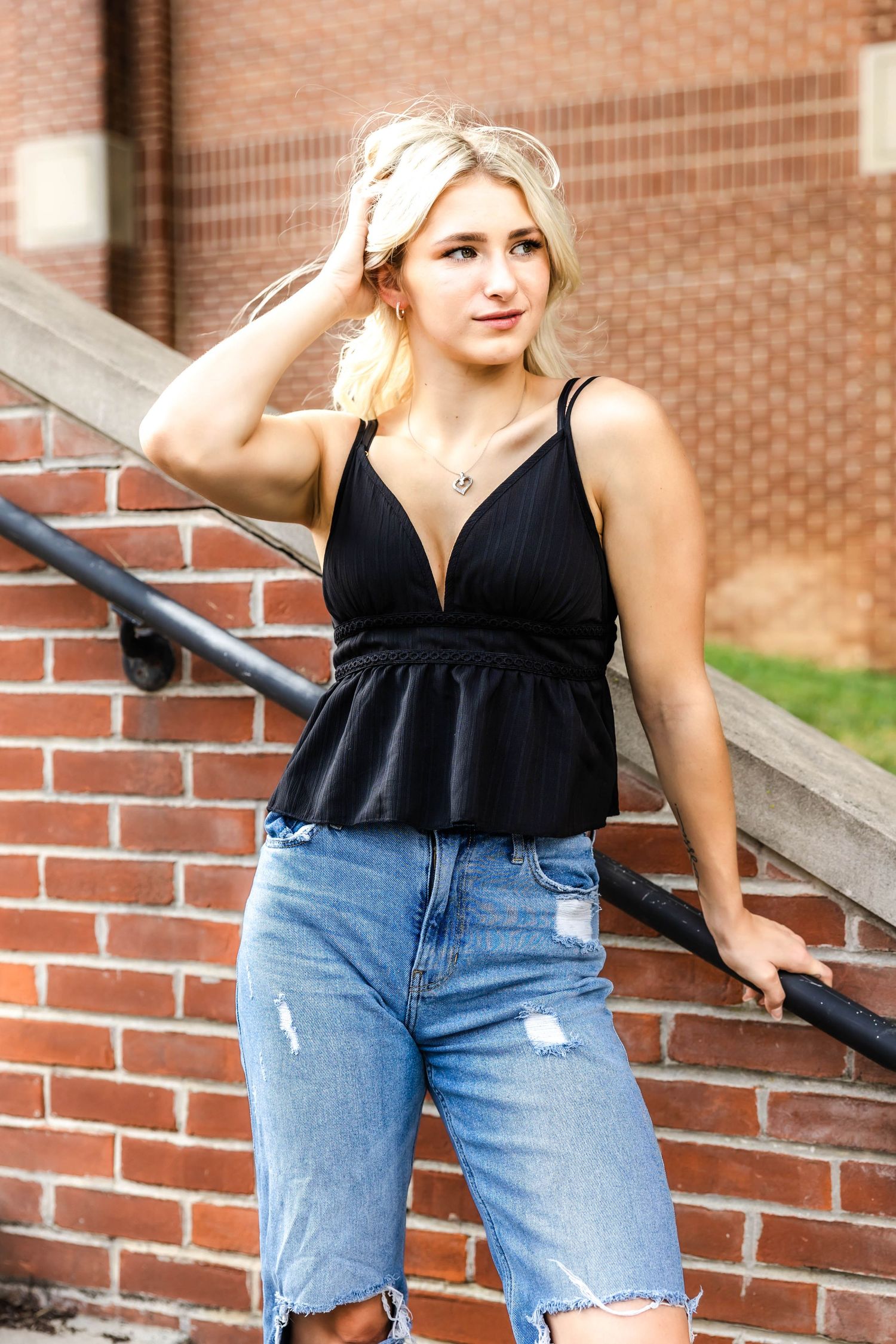 Casual summer style with black v-neck peplum top and distressed jeans by brick staircase.
