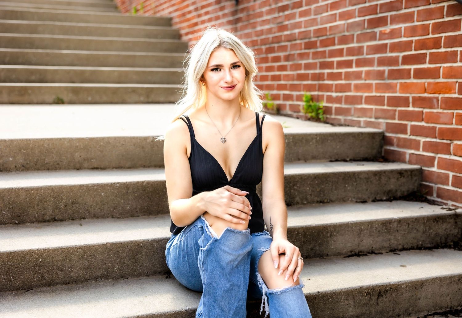 Casual portrait on brick steps wearing black tank top and distressed jeans with sandals.