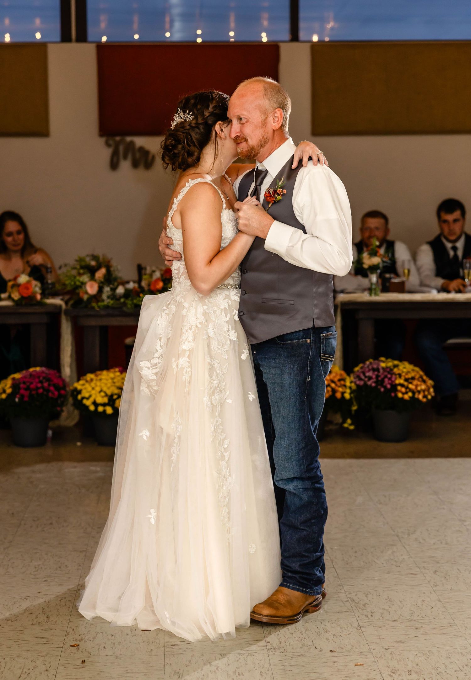 A couple shares their first dance at a wedding reception with guests seated at decorated tables.