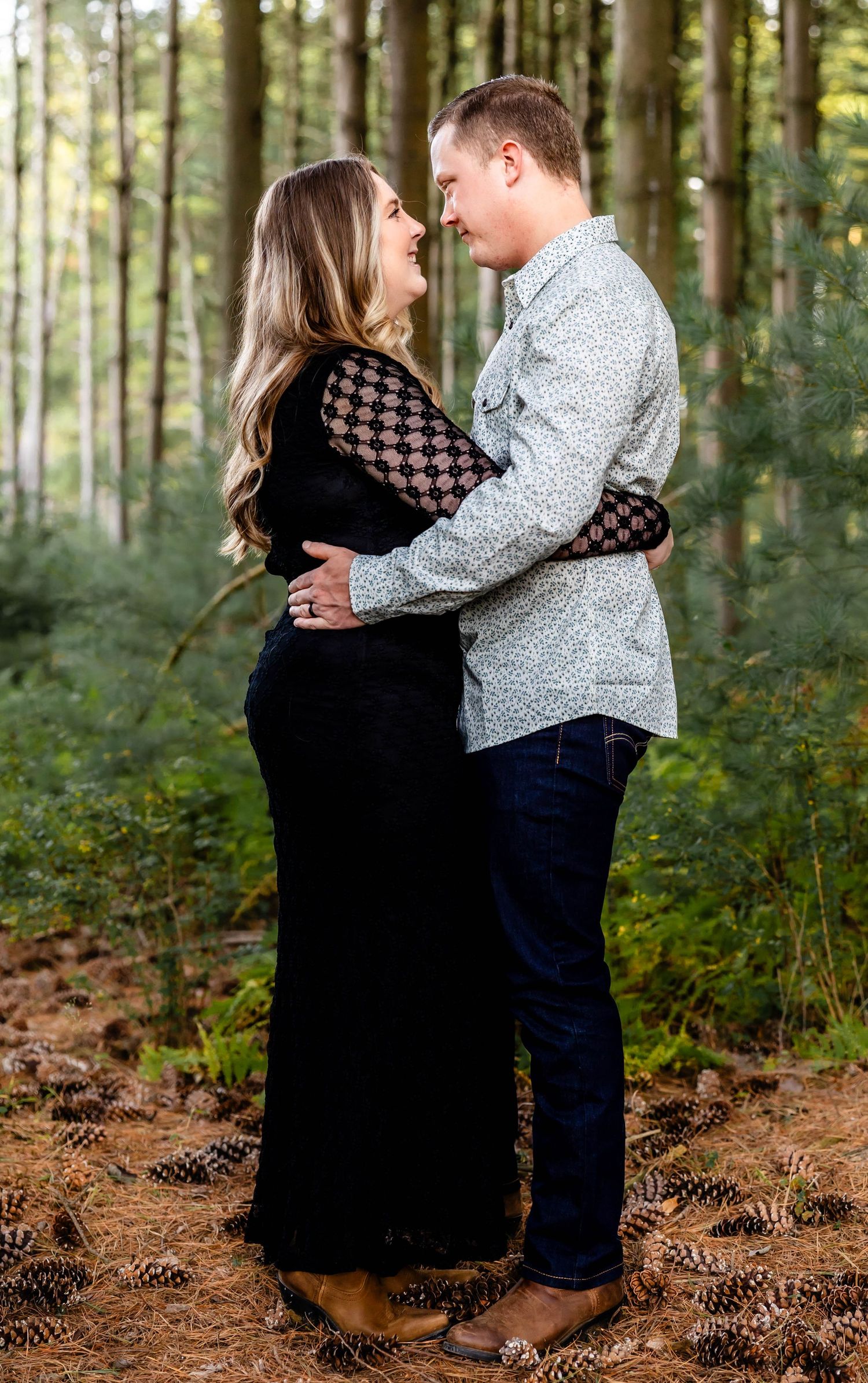 Couple in formal wear sharing an intimate embrace in a forest setting.