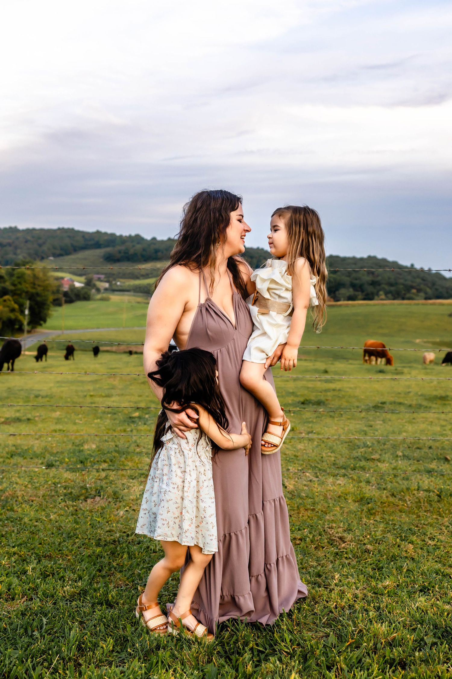 A family shares a joyful moment together in a pastoral field with grazing cattle in the background.