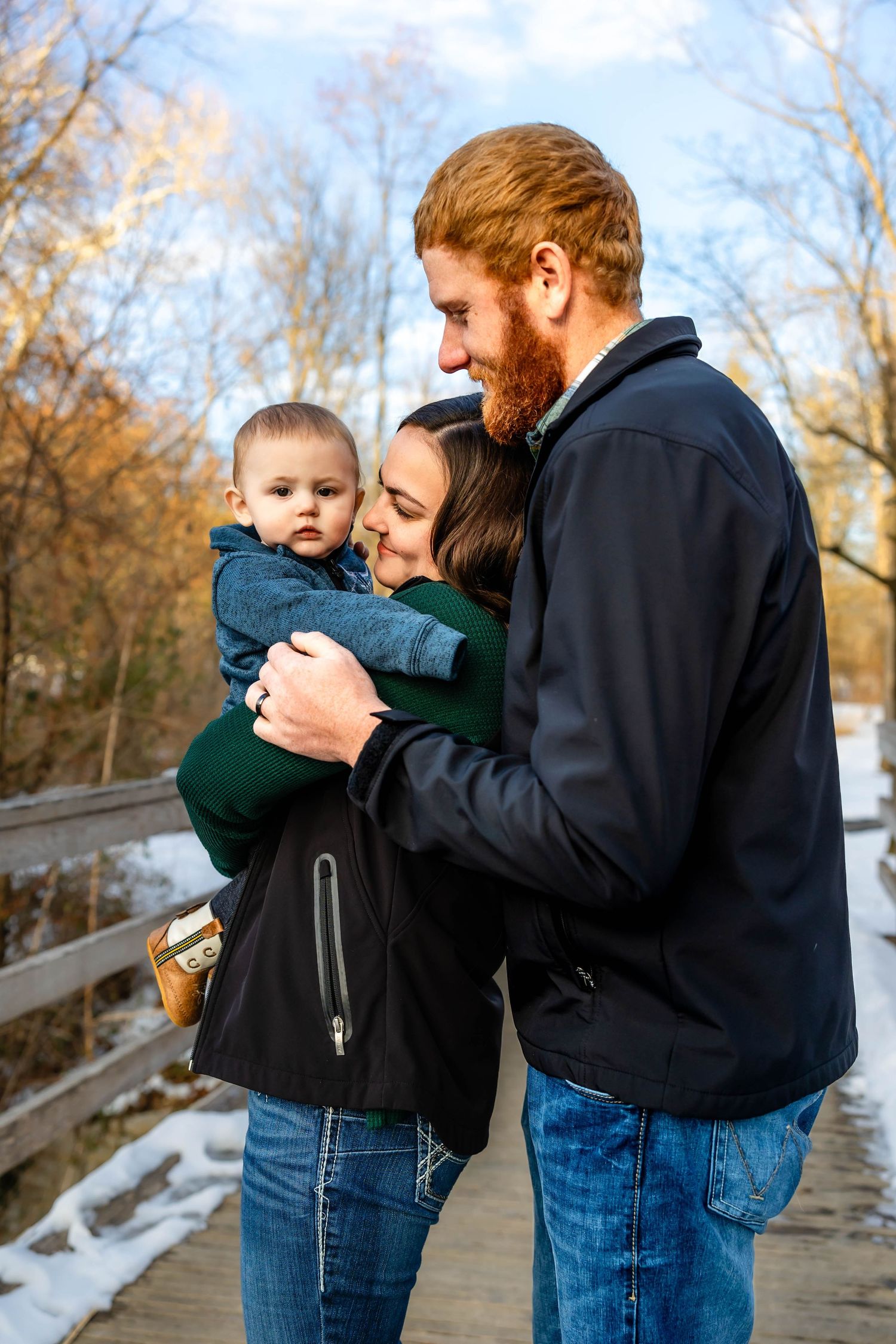 A tender family moment shared on a wooden bridge during winter with snow visible in the background.