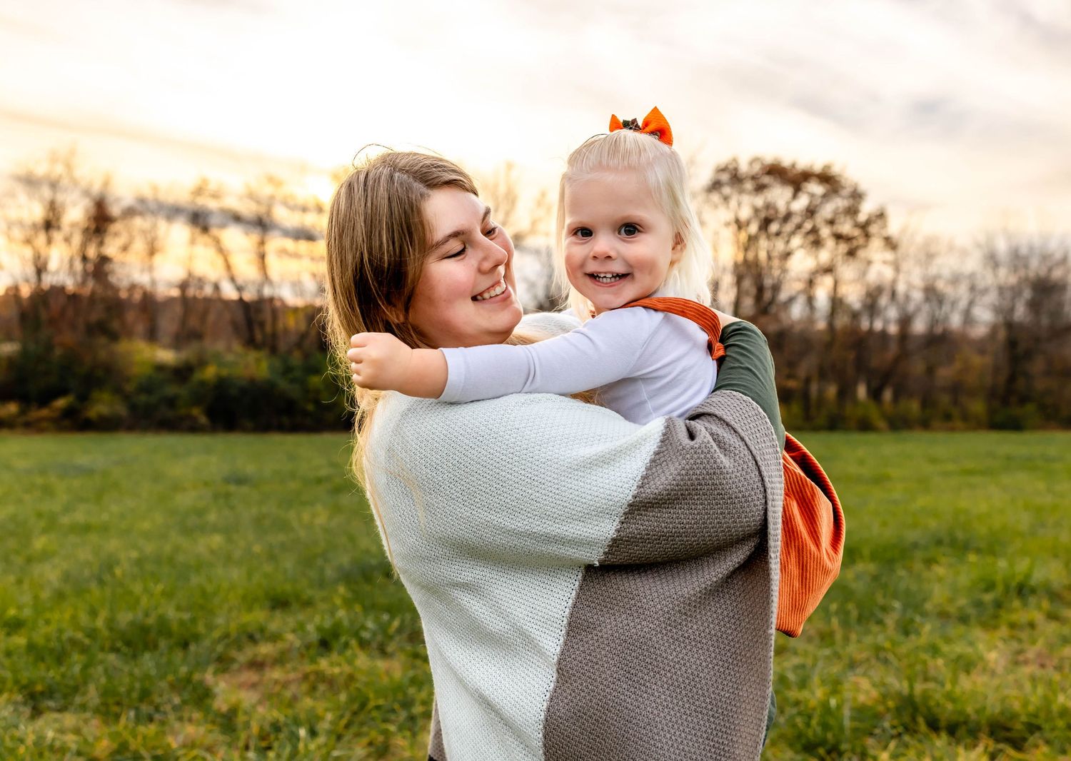 Mother and child embrace while playing in autumn field at sunset.