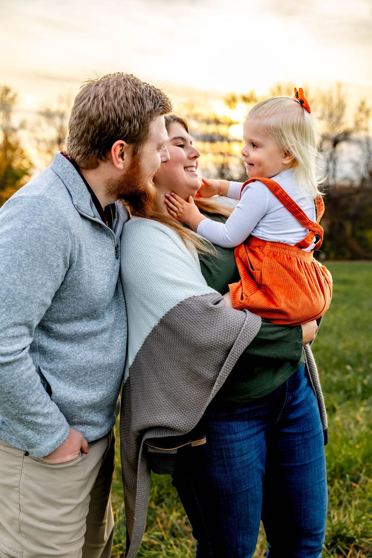 Family shares intimate moment together in field during golden hour.