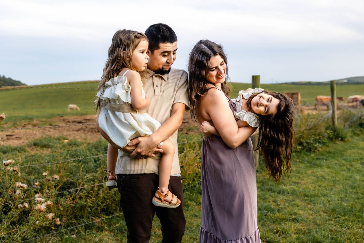 A joyful family moment captured in a grassy field with rolling hills in the background.