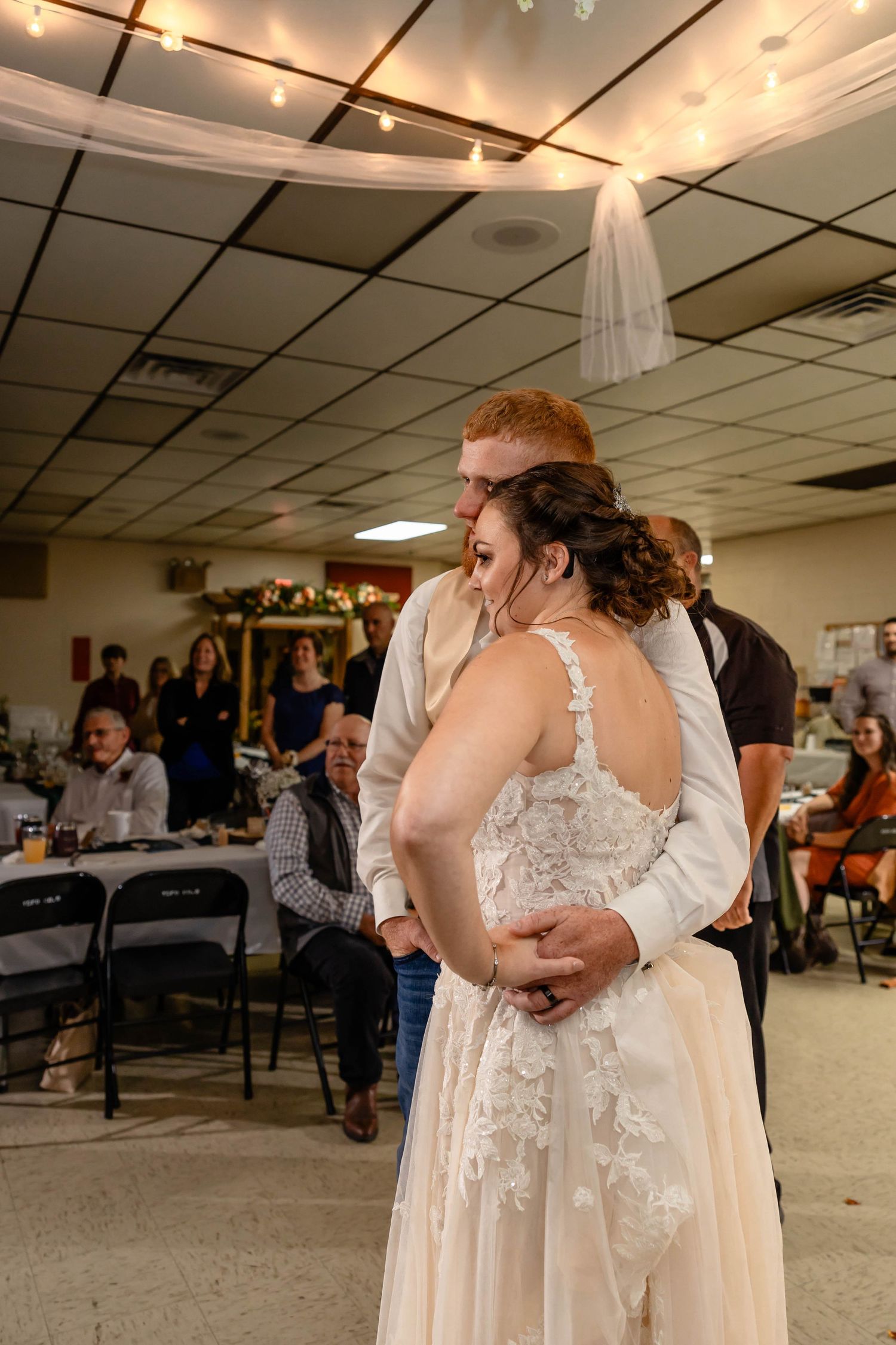 Romantic slow dance embrace during wedding reception under dimly lit ceiling.