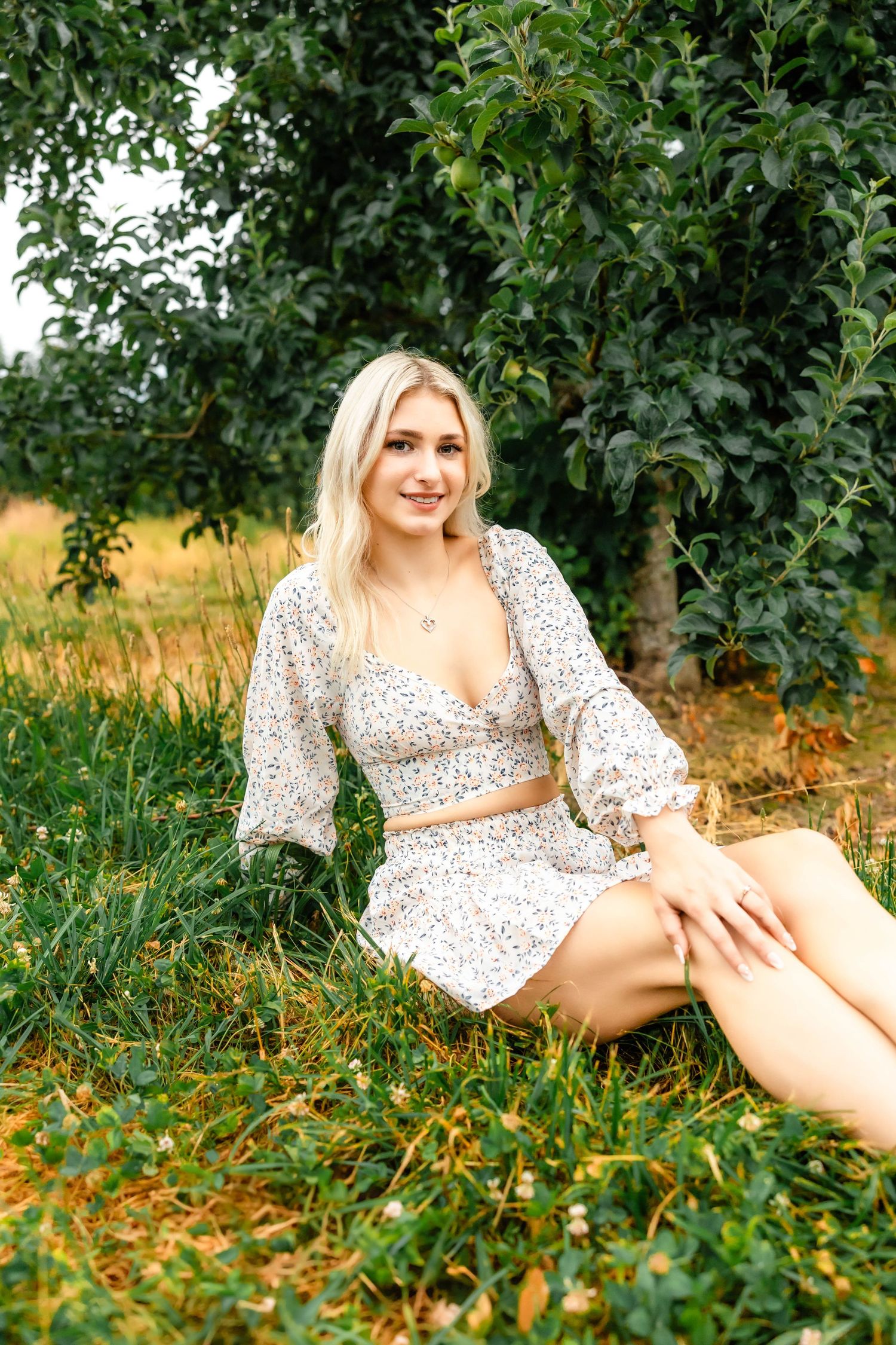 Outdoor lifestyle photography featuring a white floral two-piece outfit in an orchard setting.