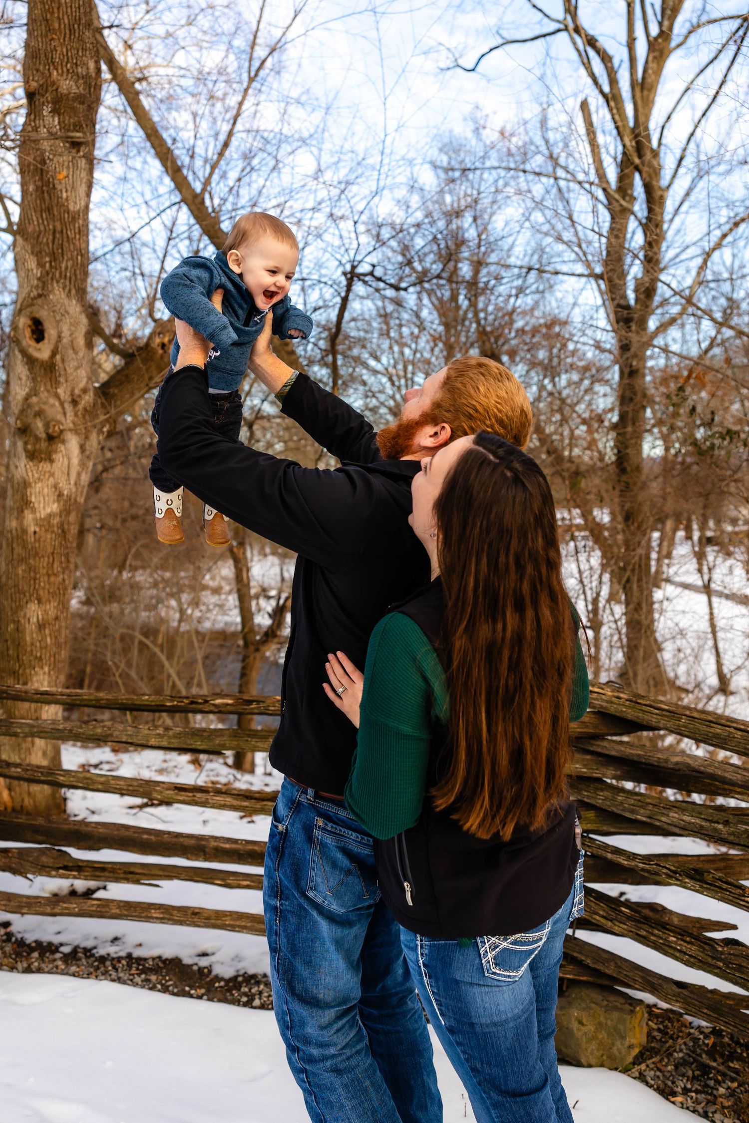 Joyful winter moment as parents lift small child in air against snowy backdrop.