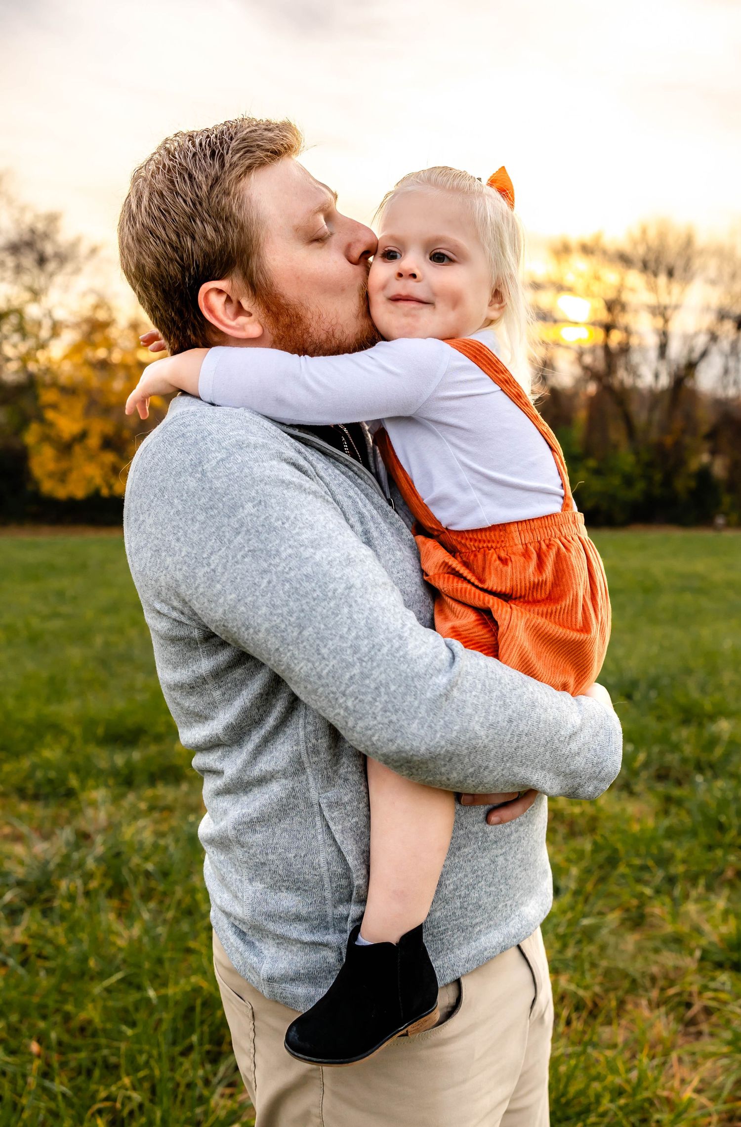 Sweet outdoor portrait showing familial affection with autumn trees in the background.
