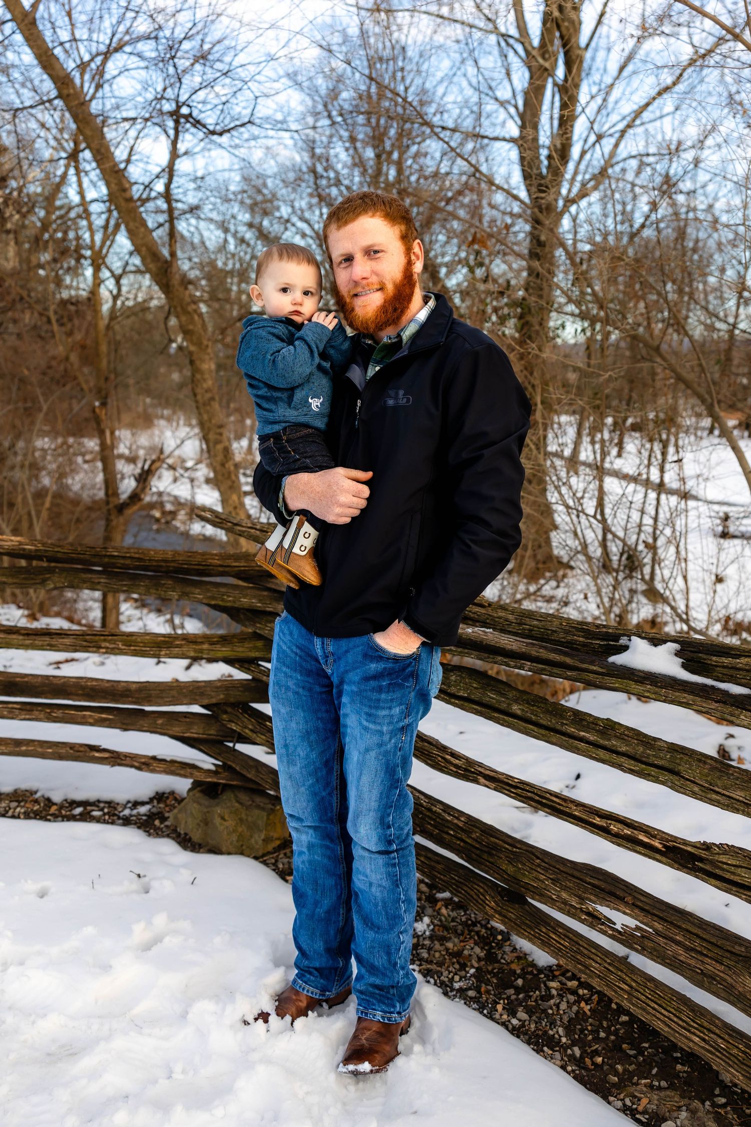 Winter portrait in front of snow-covered wooden fence with father holding child.
