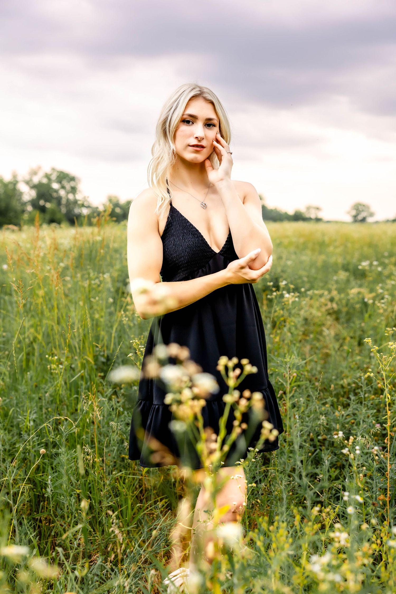 Black v-neck sundress shown in an artistic portrait among wildflowers and tall grass.