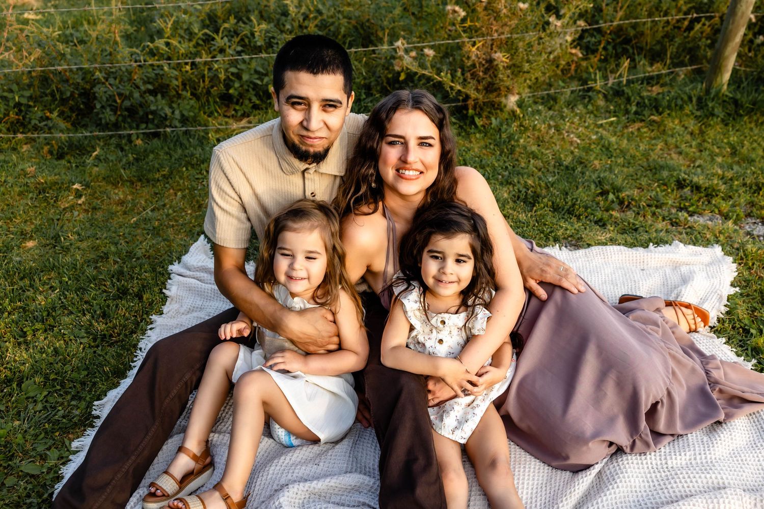 A family enjoys a cozy picnic together on a blanket in a sunny garden setting.