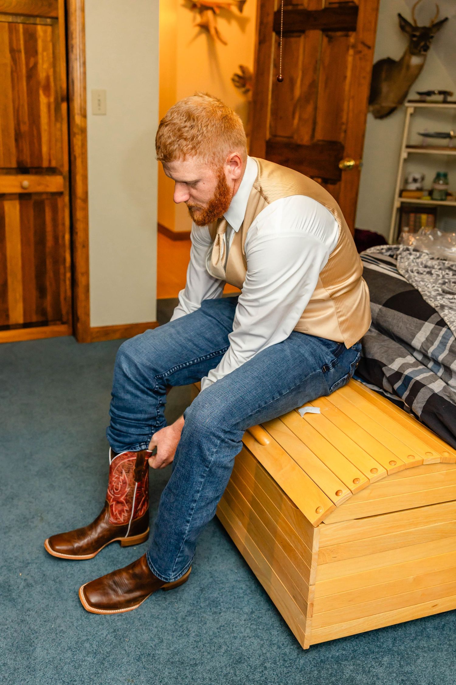 Someone puts on brown leather boots while sitting on a wooden chest.