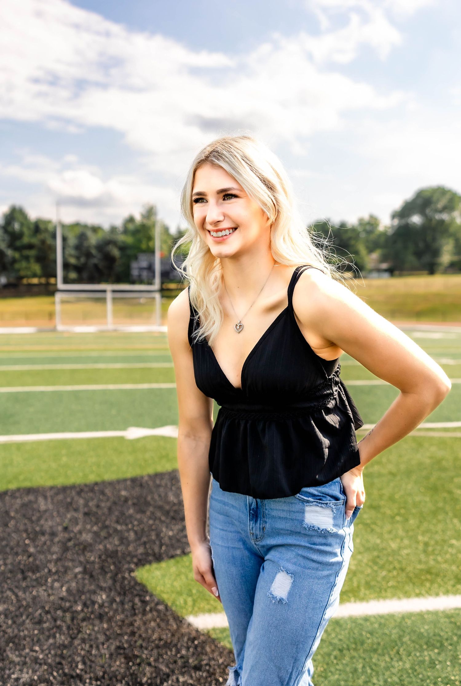 A casual fashion portrait on a football field featuring a black peplum top and distressed jeans.