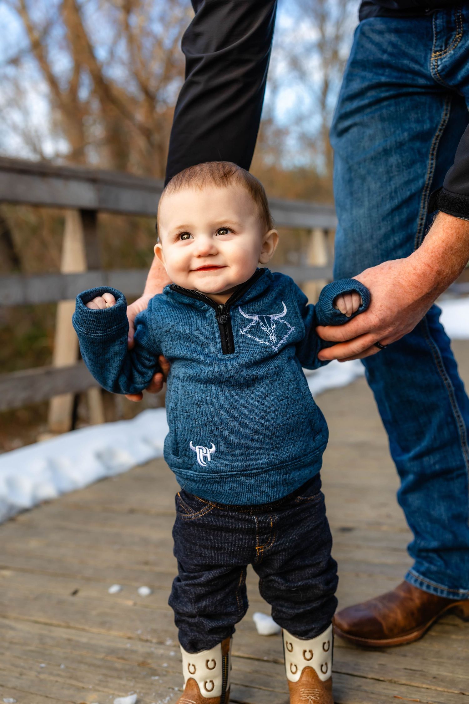 Happy toddler in blue sweater smiling while standing on wooden deck.