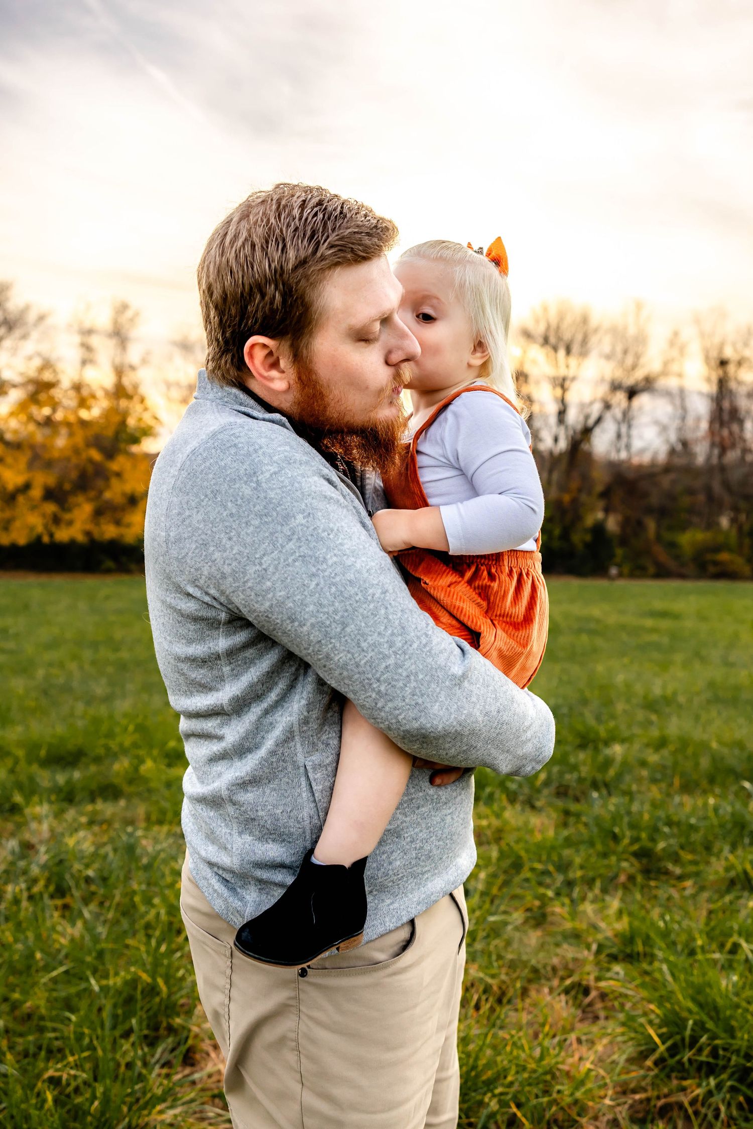 Sweet family moment captured in golden hour lighting with playful kisses and orange autumn attire.