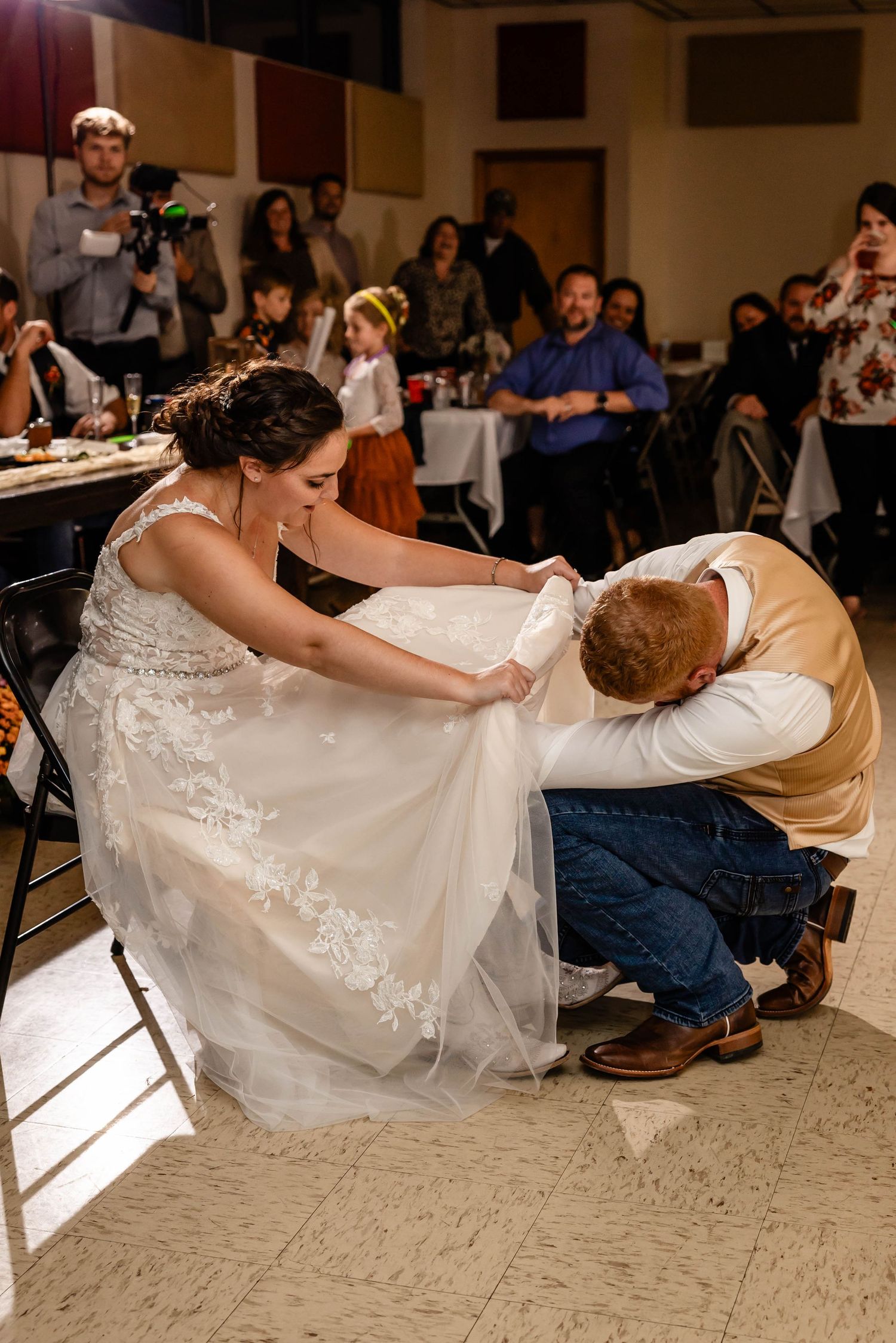 A playful wedding tradition moment during the reception with guests watching in the background.