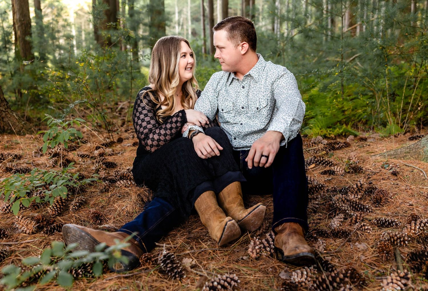 Couple in coordinated outfits sharing intimate moment while sitting in pine forest.