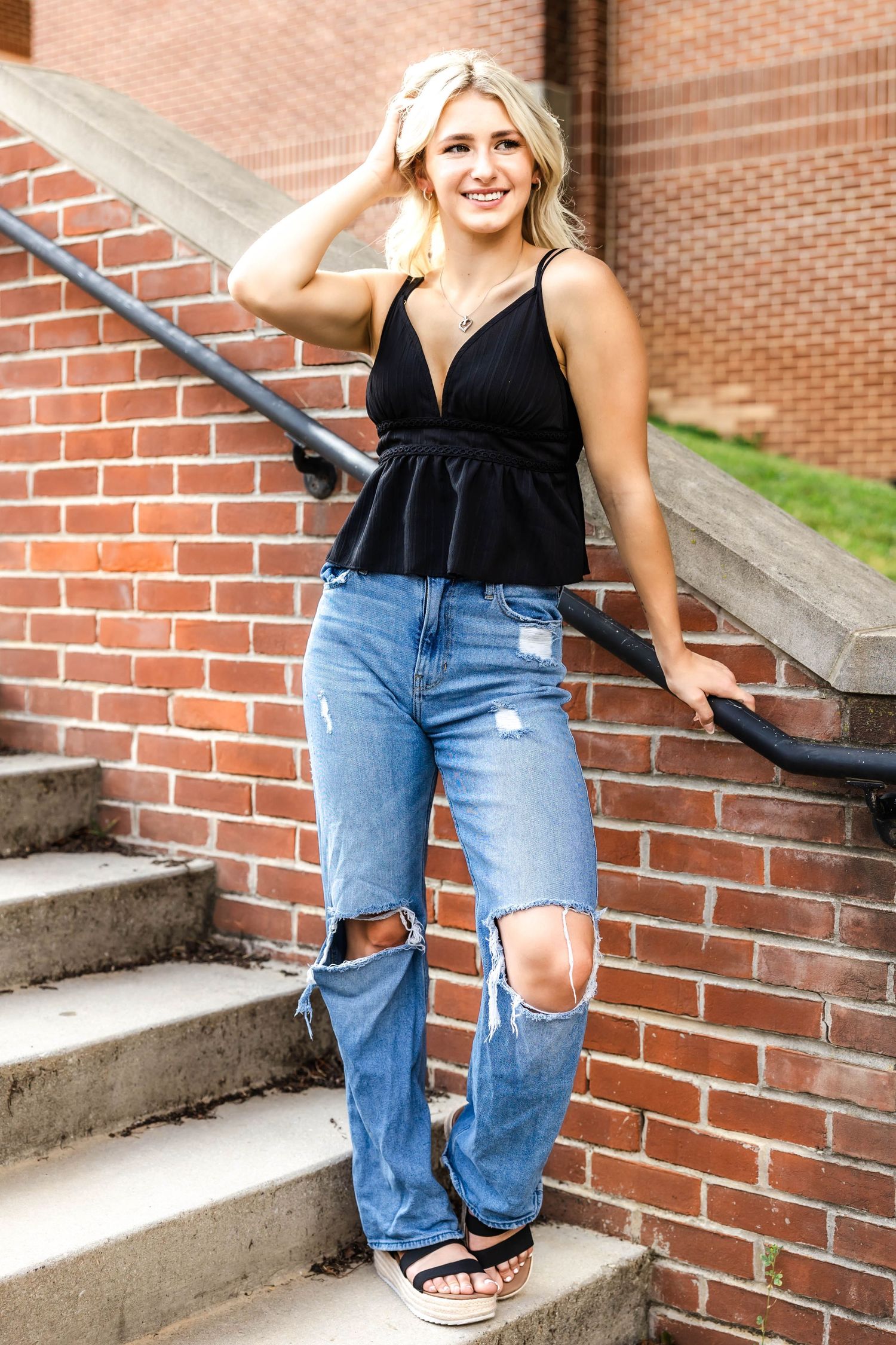 Summer fashion portrait featuring black peplum tank and ripped jeans on brick steps.