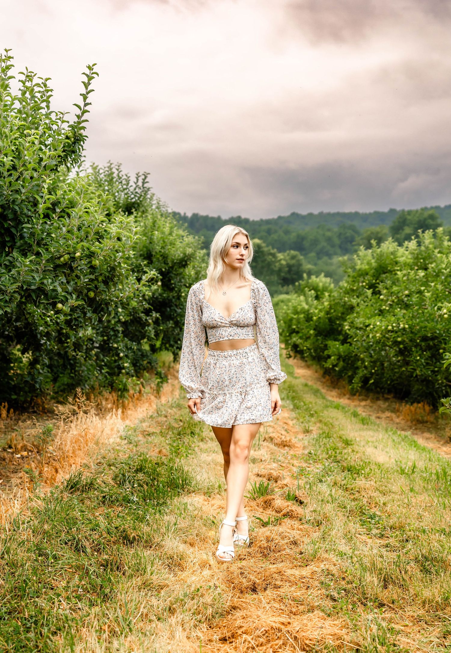 Romantic summer photoshoot featuring a white floral crop top and skirt set in an apple orchard.