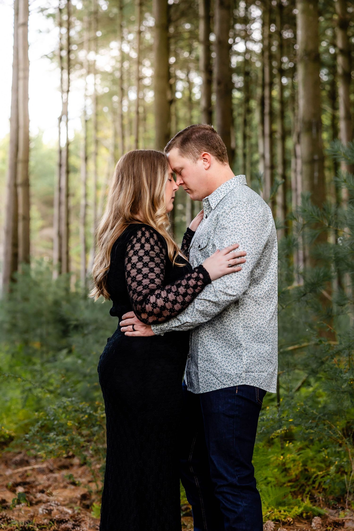 Romantic forest engagement photo with couple embracing among pine trees.