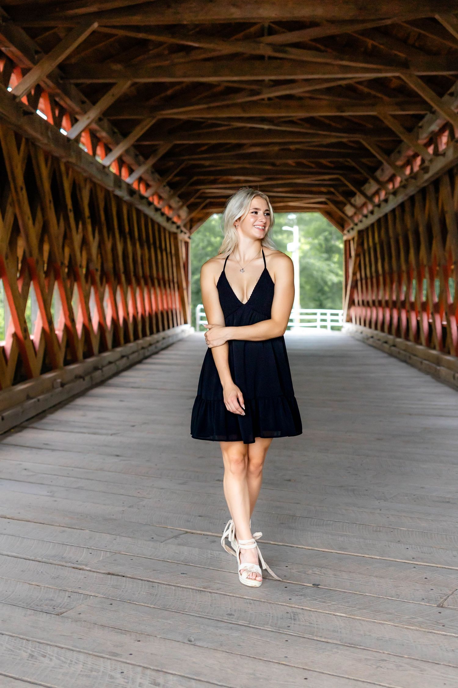 Elegant black sundress and heels worn in a wooden covered bridge walkway.