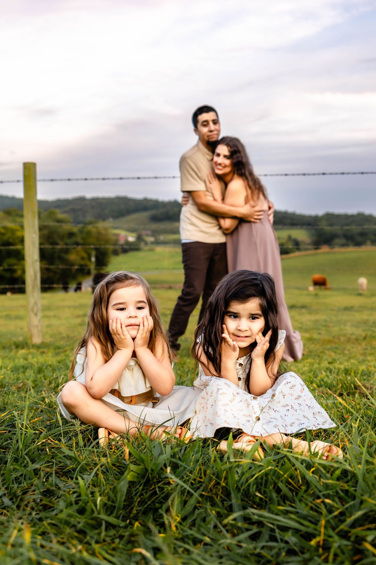 A candid family photo in a pastoral setting with children laying in grass and adults embracing behind.