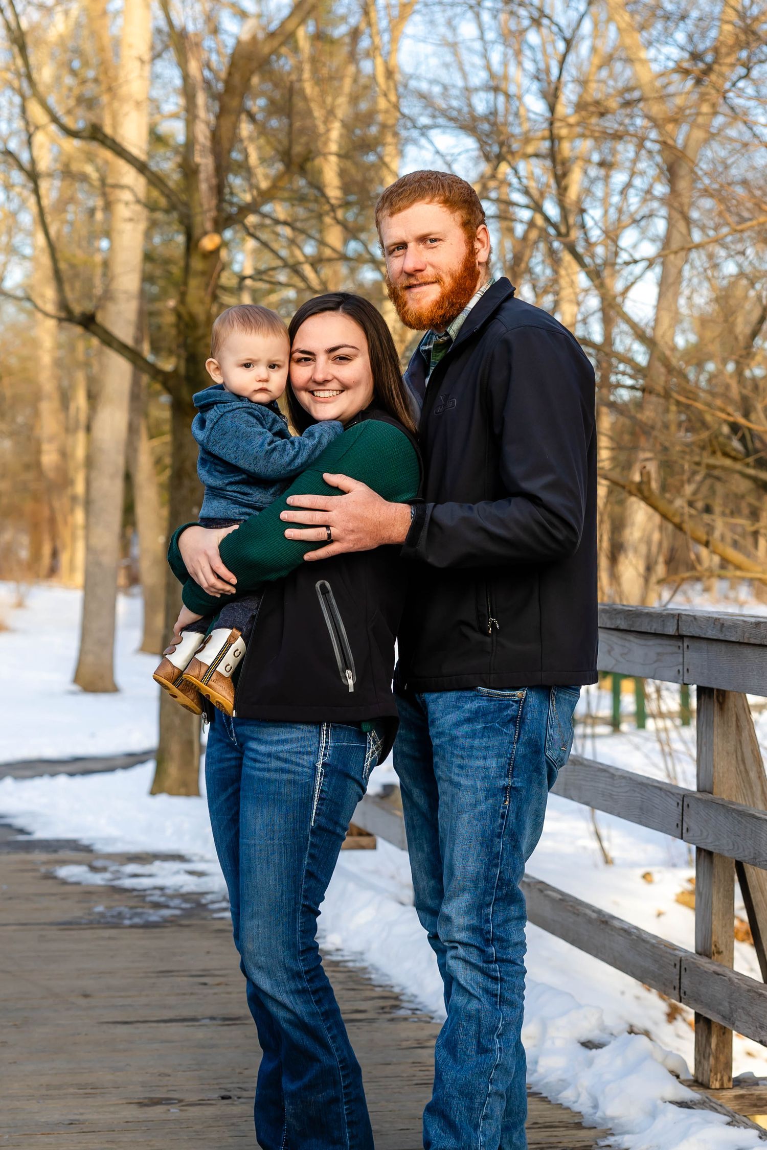 Family portrait on wooden boardwalk with snowy winter forest backdrop.