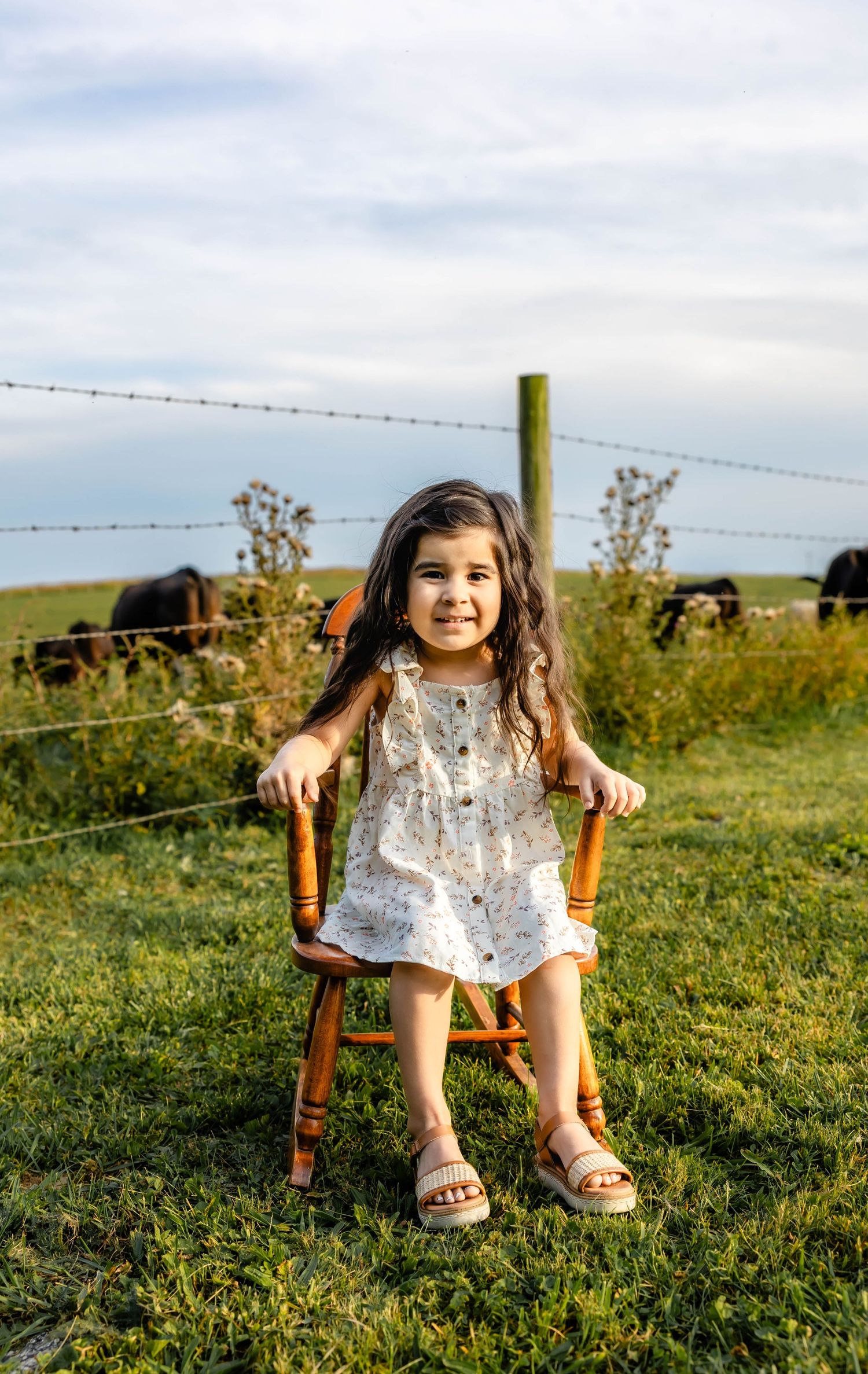 A cheerful moment captured of a young person on a wooden chair against a pastoral farm backdrop.