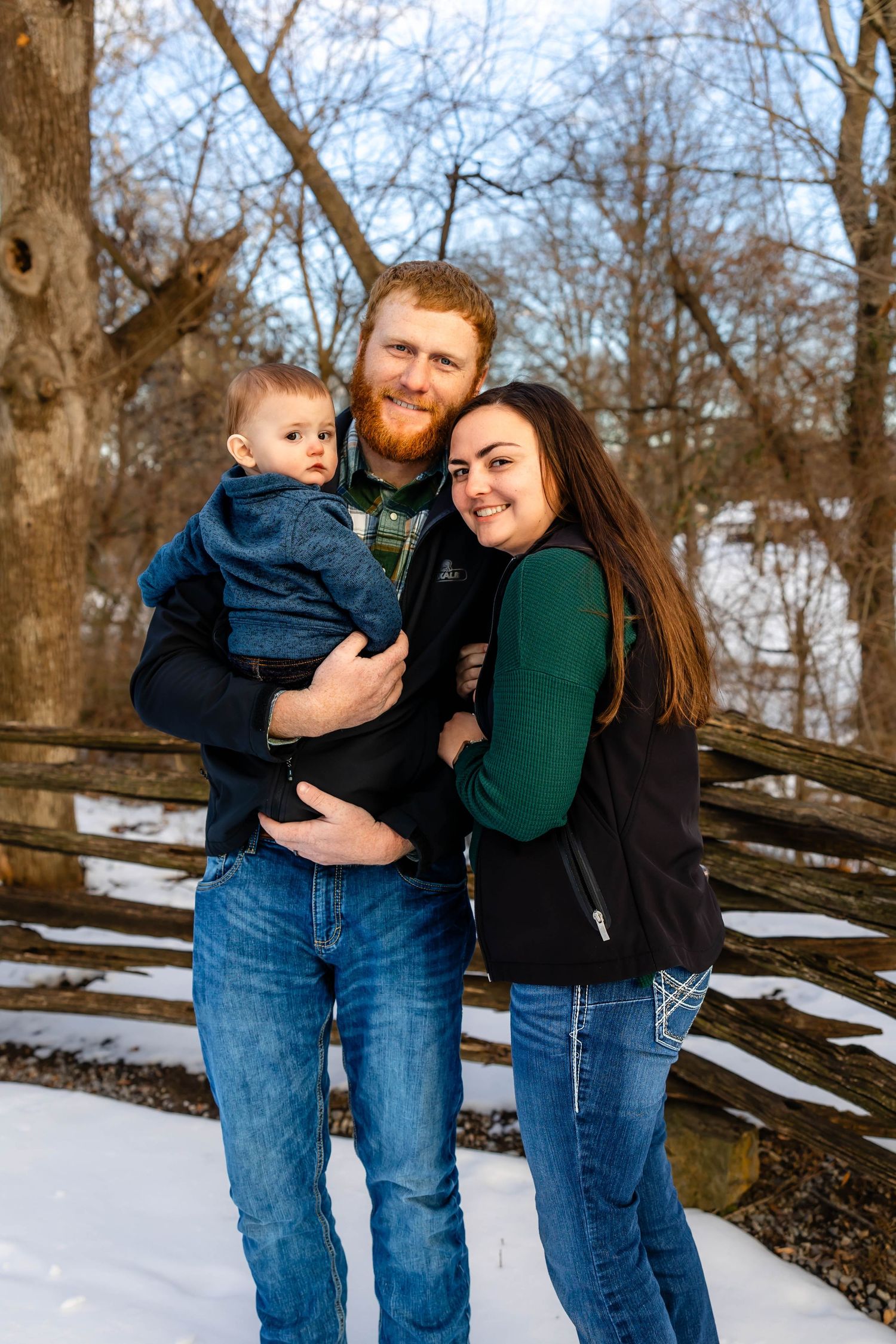Loving family portrait on wooden bridge during winter with snow in background.