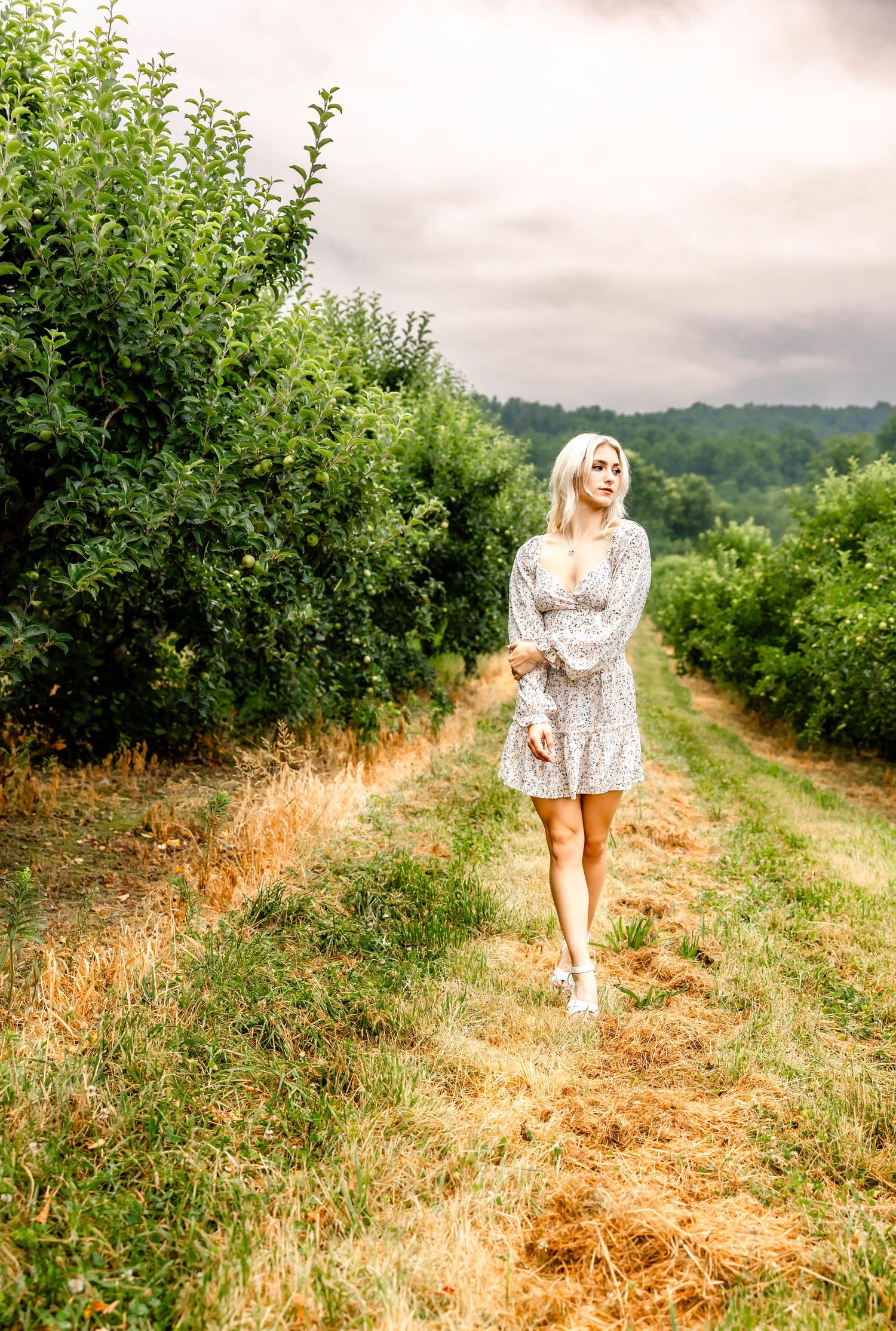 Summer fashion photography in an orchard featuring a delicate white floral dress.