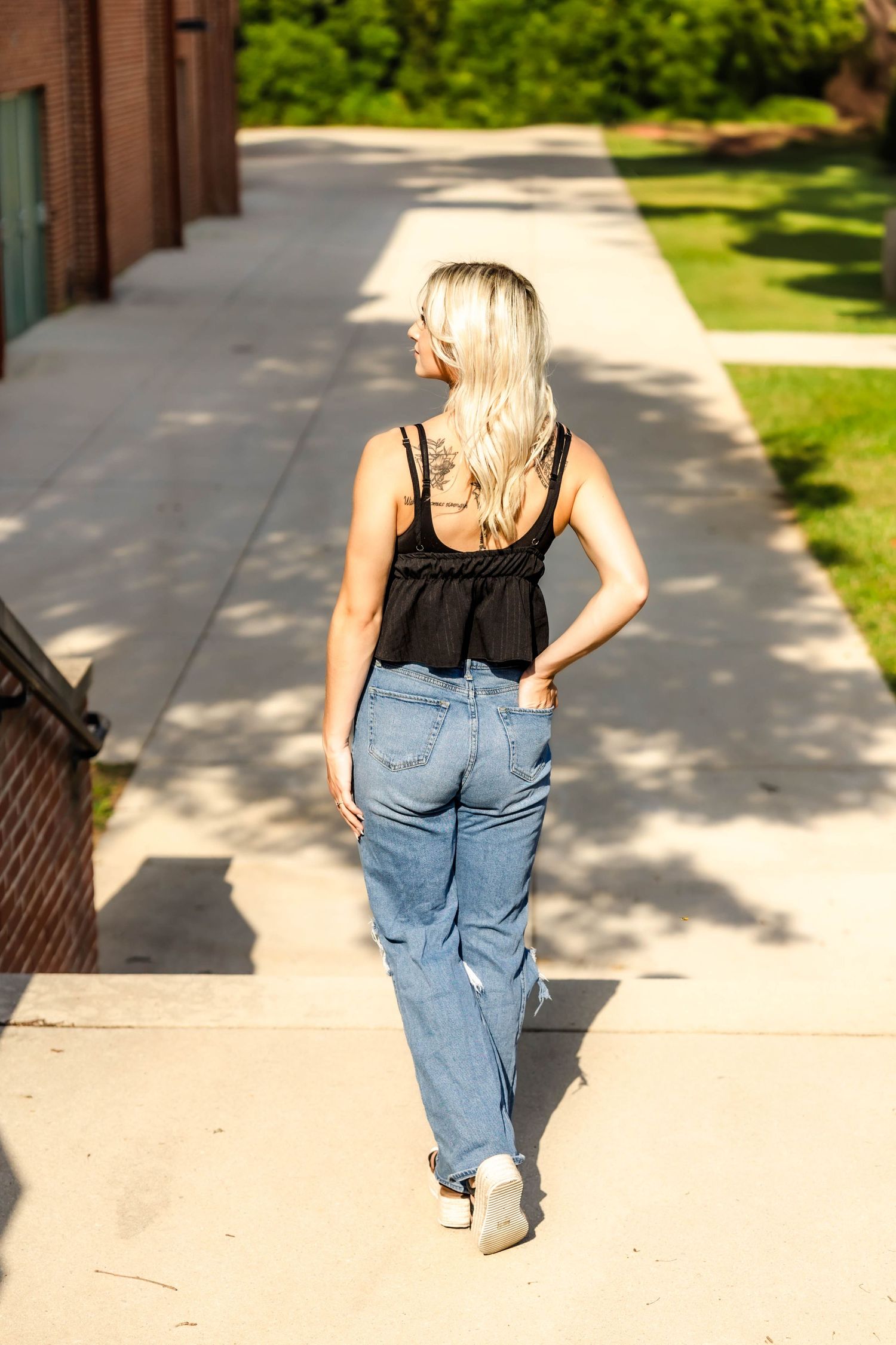 Back view of casual summer outfit walking along sunny brick building path.
