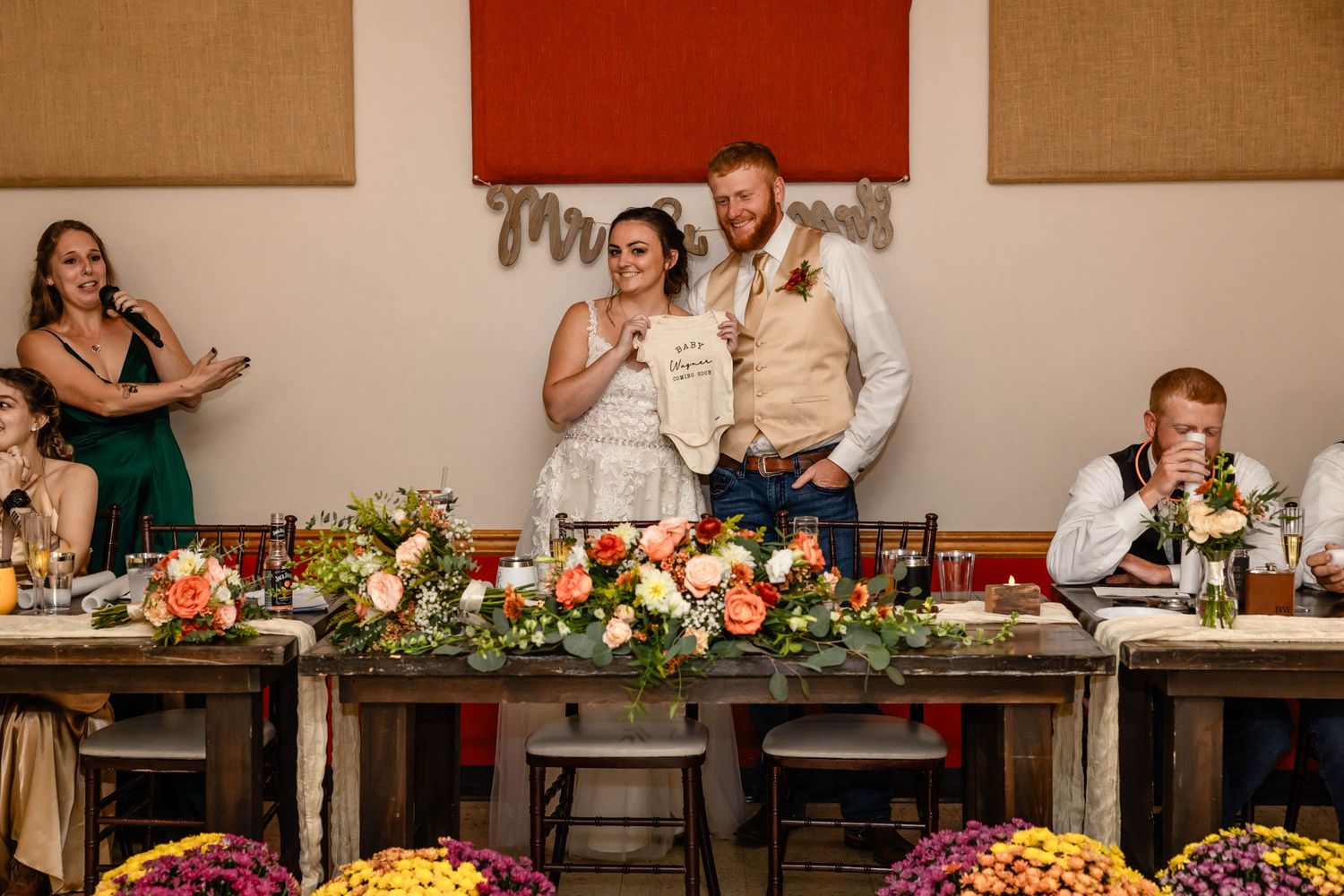 Wedding reception head table decorated with colorful floral arrangements and rustic decor.