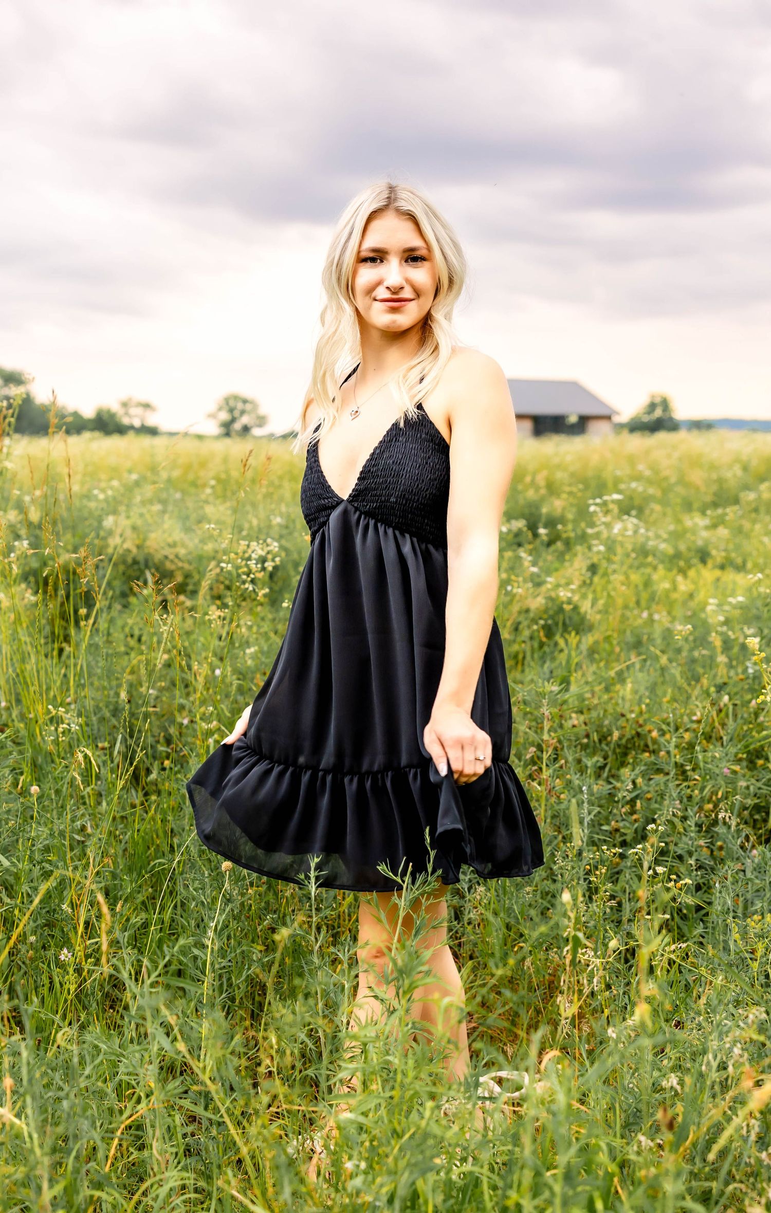 Flowy black dress with v-neck and ruffle detail shown in a field of summer wildflowers.