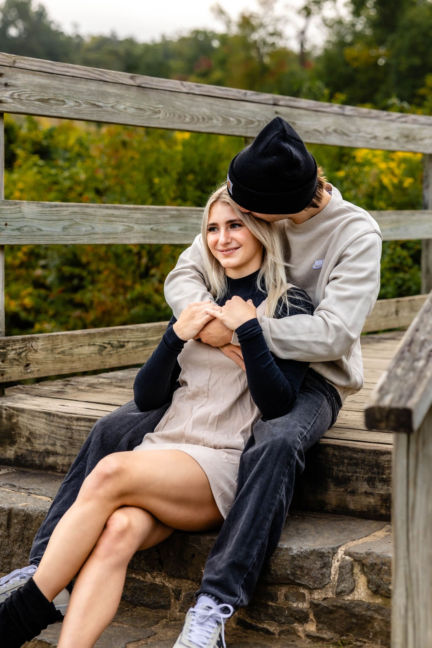 Couple cuddling on rustic wooden bridge steps during fall season.