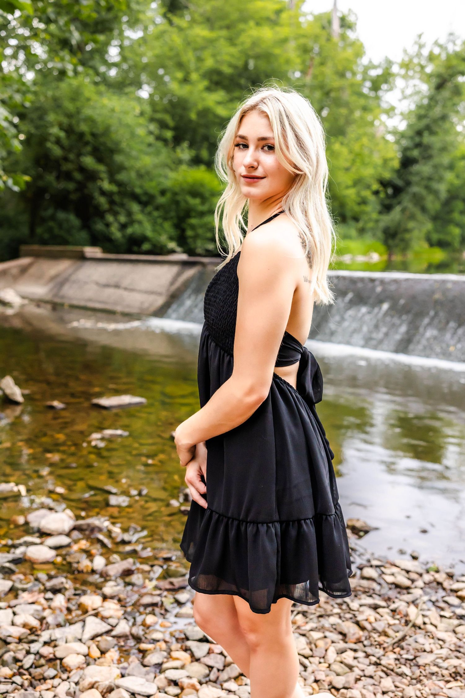 A flowy black dress with ruffle detail is modeled near a concrete waterfall structure.