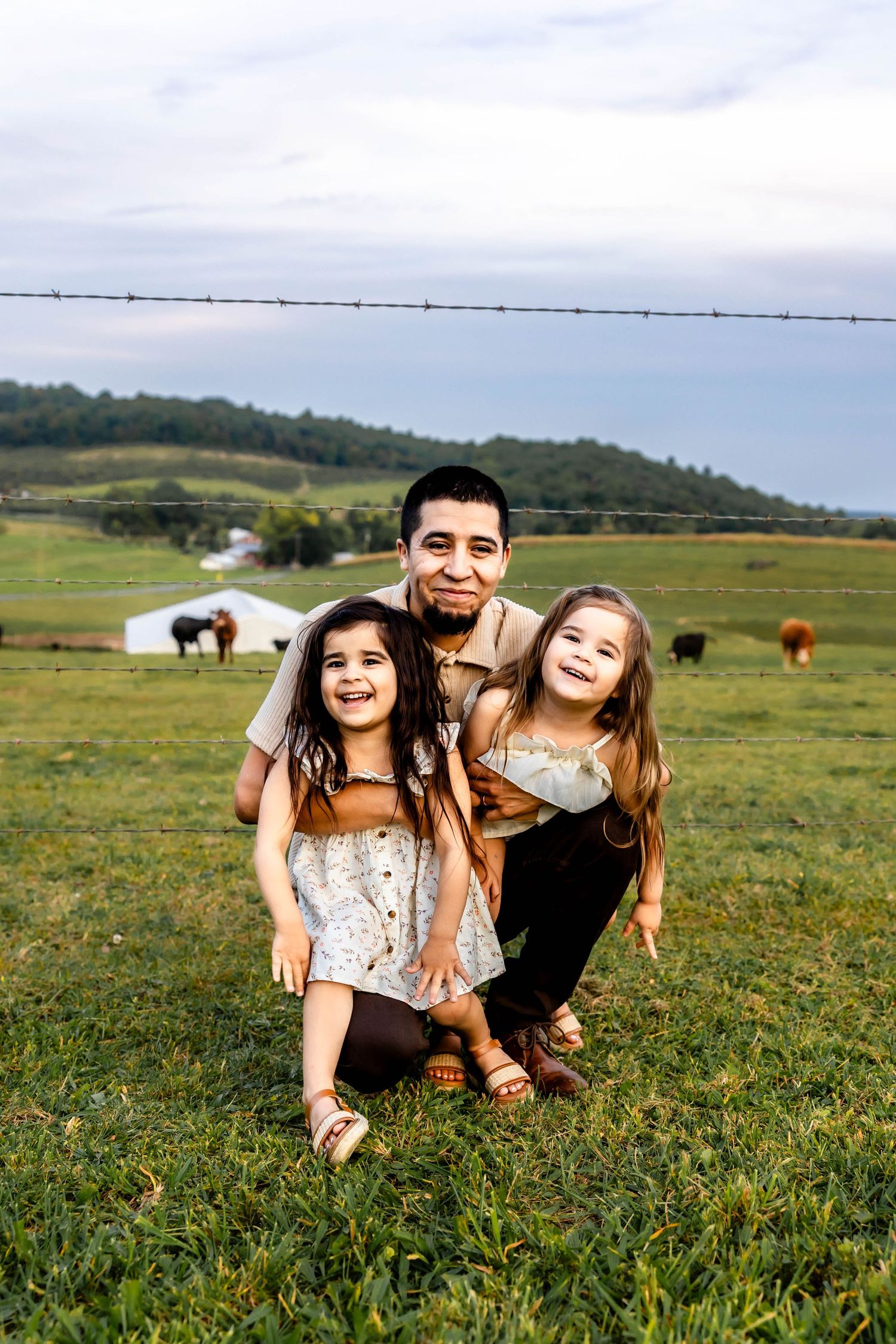 A cheerful group poses playfully in a grassy field with mountains and cattle in the background.