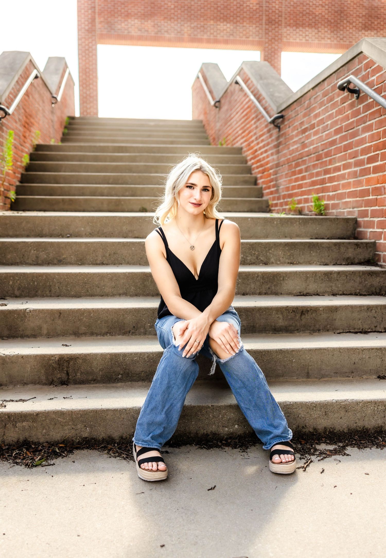 Casual outdoor portrait on brick staircase wearing black tank and distressed denim.