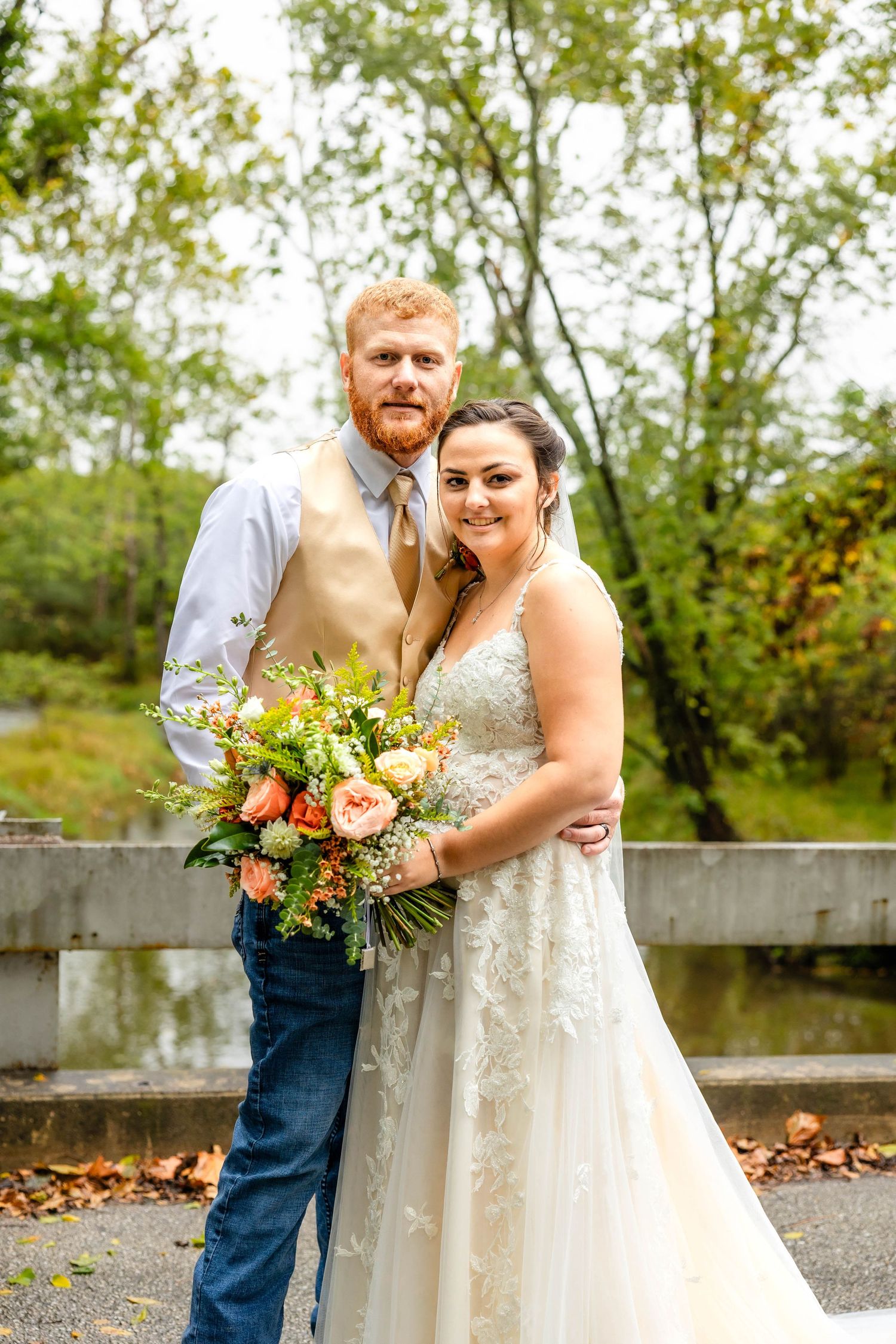 Newlyweds pose outdoors on an autumn day with a beautiful peach floral bouquet.