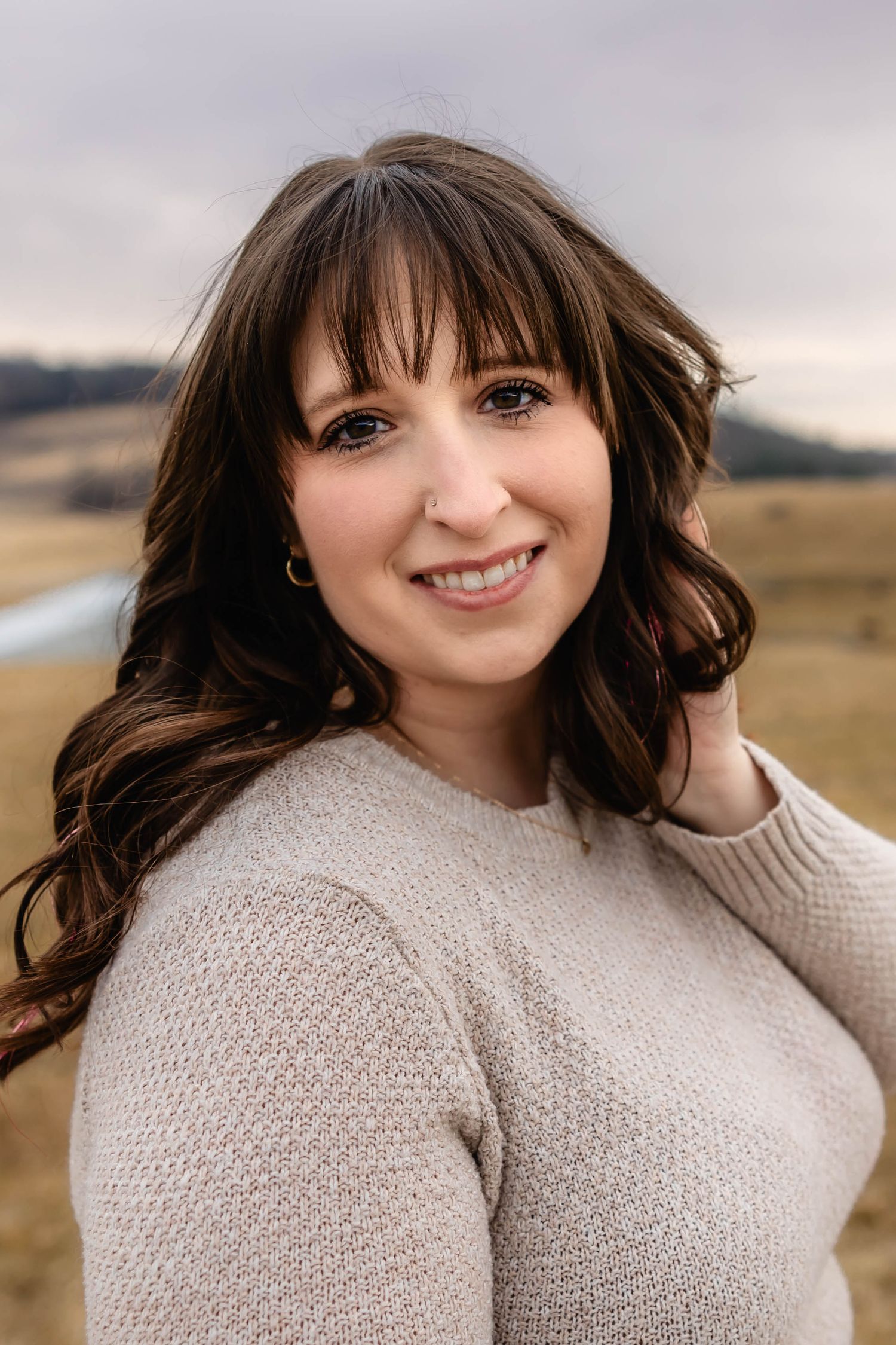 A person in a cozy sweater smiles warmly against an autumn mountain backdrop.