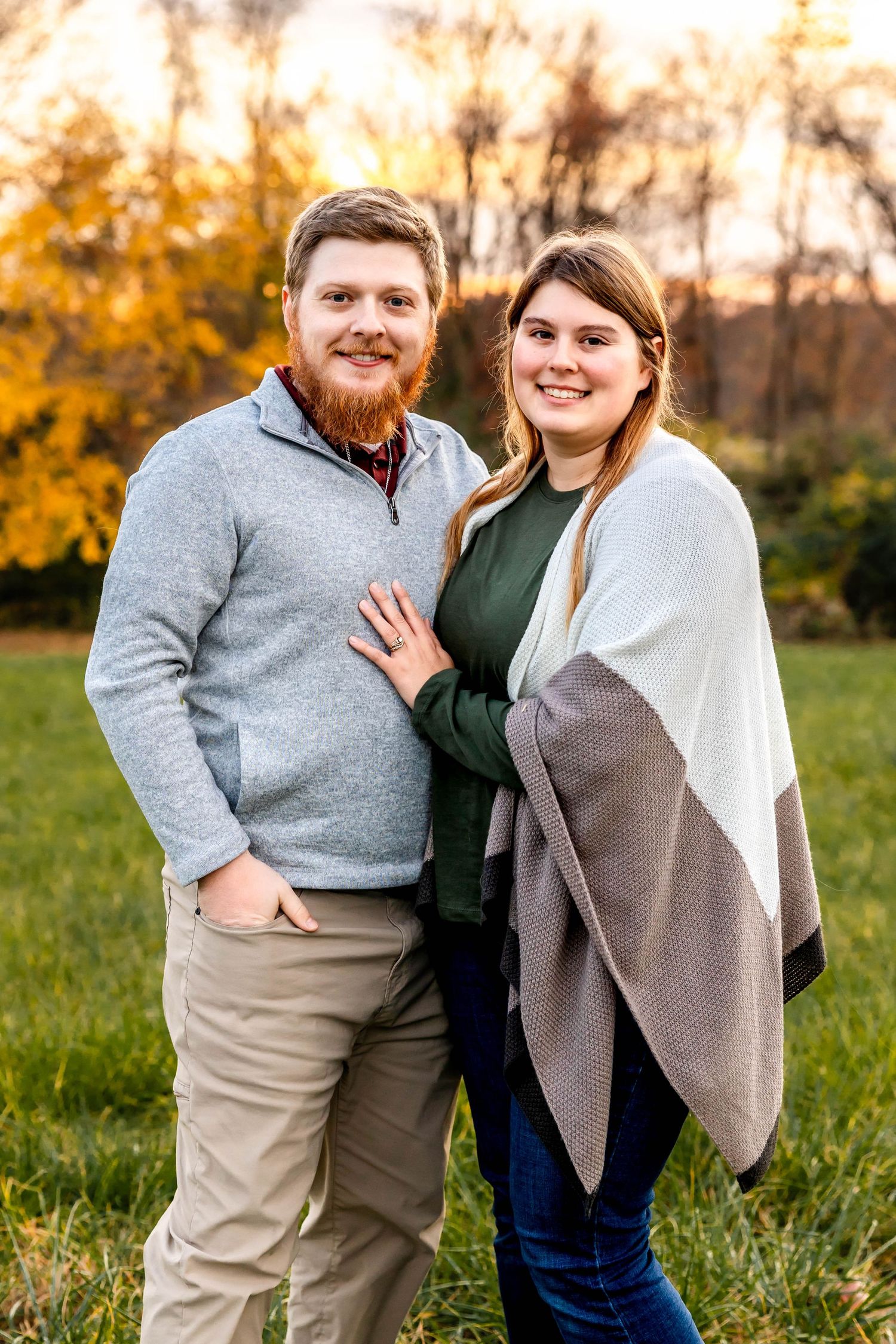 A couple poses together during autumn, surrounded by golden foliage at sunset.